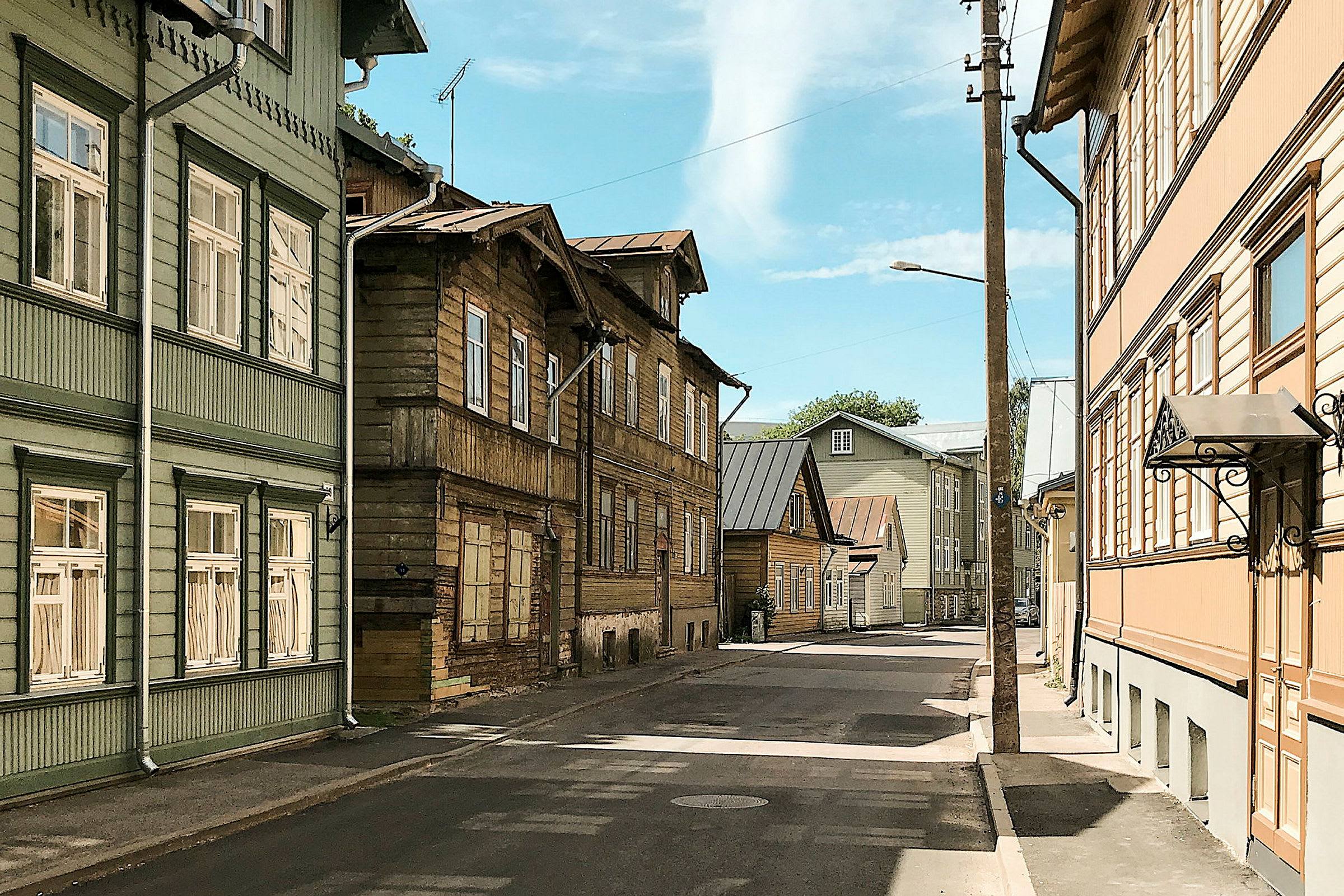 En gate omgitt av hus i tre med forskjellige farger, blå himmel ses i bakgrunnen. (AI-generert tekst)