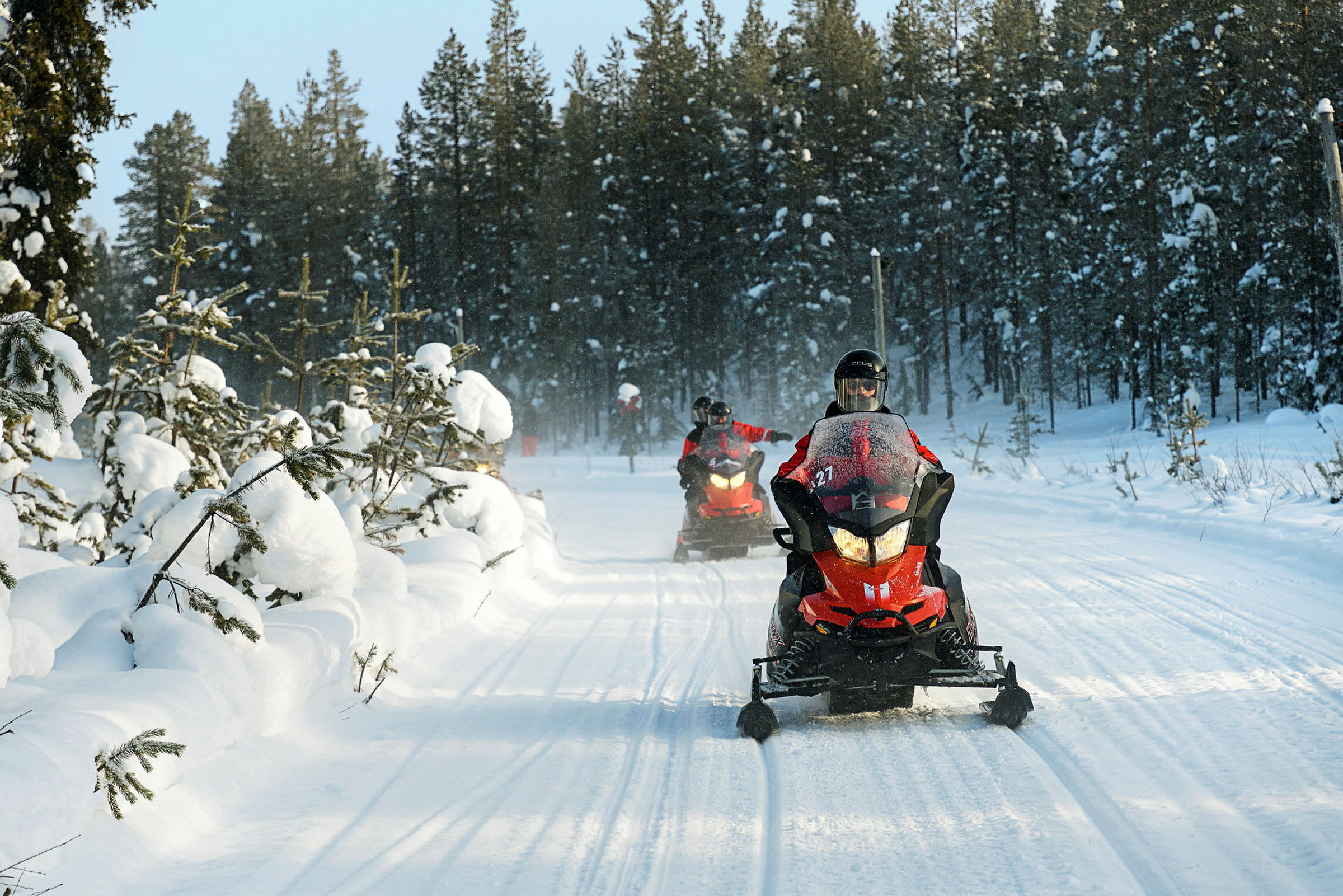 Snøscootere kjører på en snødekt vei omgitt av skog. (AI-generert tekst)