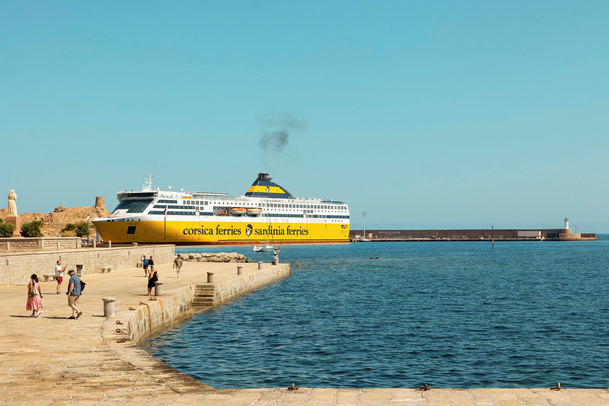 En gul og hvit ferge fra Corsica Ferries ligger ved brygga, med mennesker som går på kaianlegget og havet synlig i forgrunnen. (AI-generert tekst)