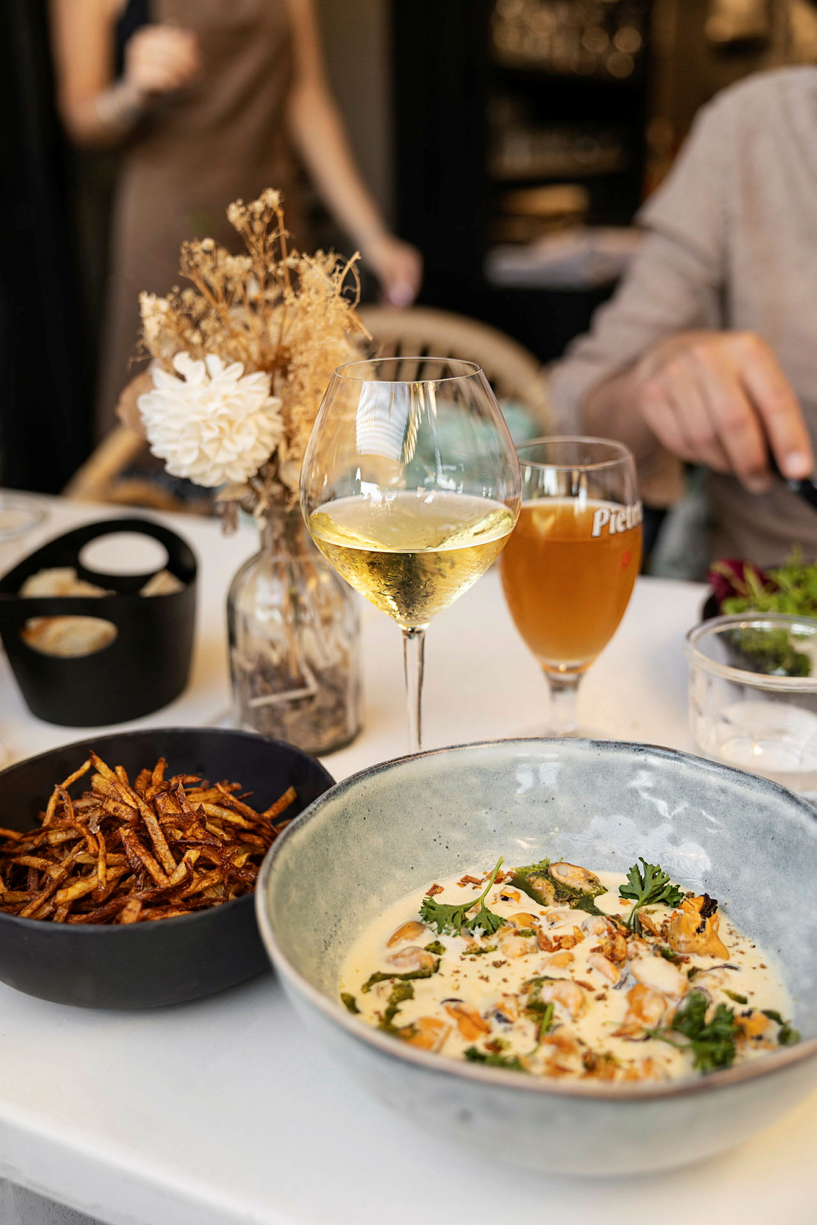 En tallerken med mat, et glass hvitvin og en bolle med pommes frites på et bord. (AI-generert tekst)