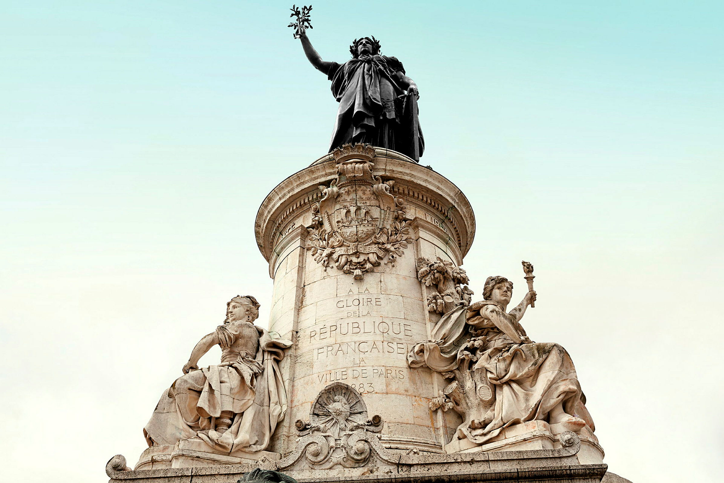 Statue med detaljerte kunstverk og inskripsjoner på en steinsokkel med klar himmel i bakgrunnen. (AI-generert tekst)
