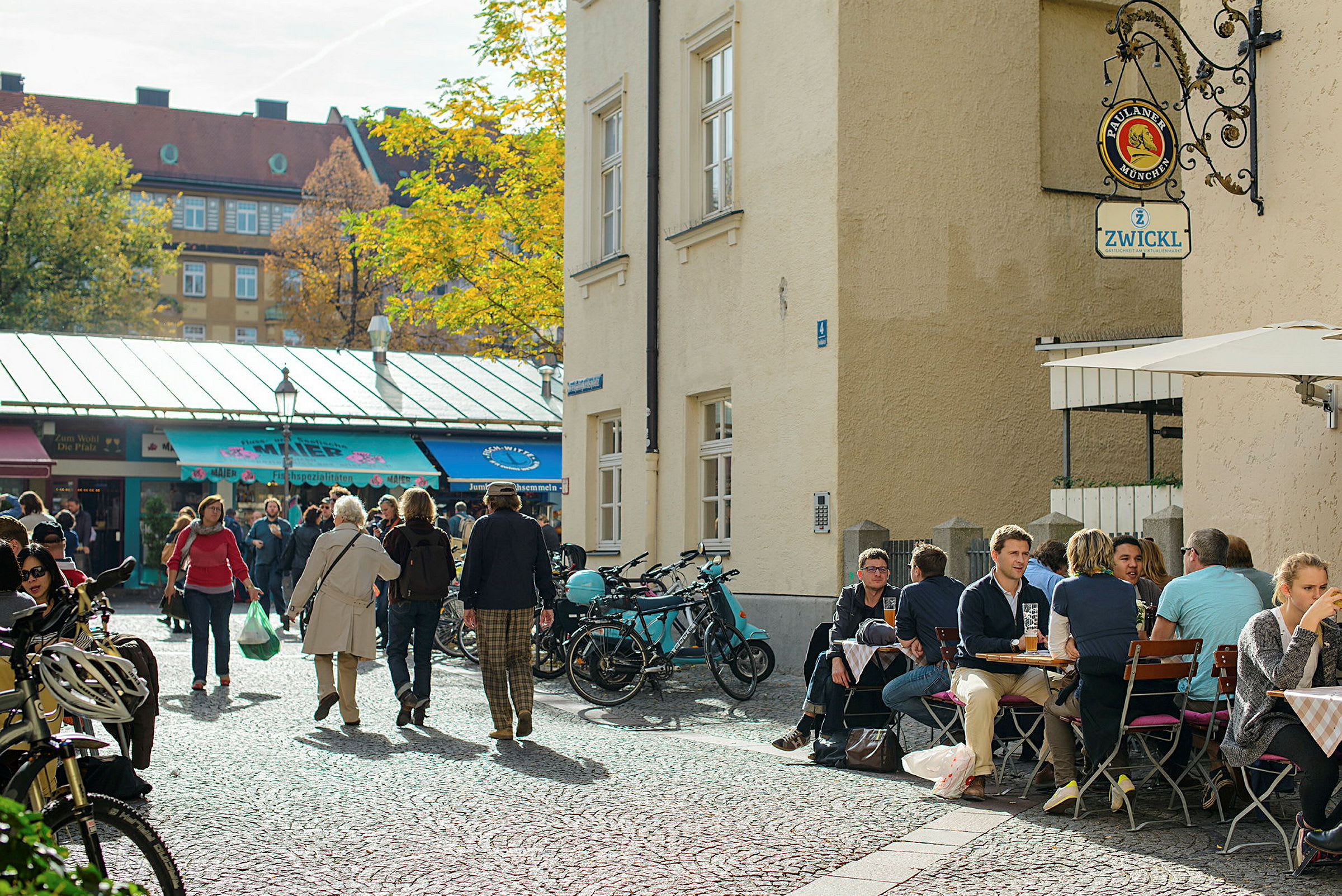 Et torg med mennesker, sykler og en kafé med uteservering. (AI-generert tekst)