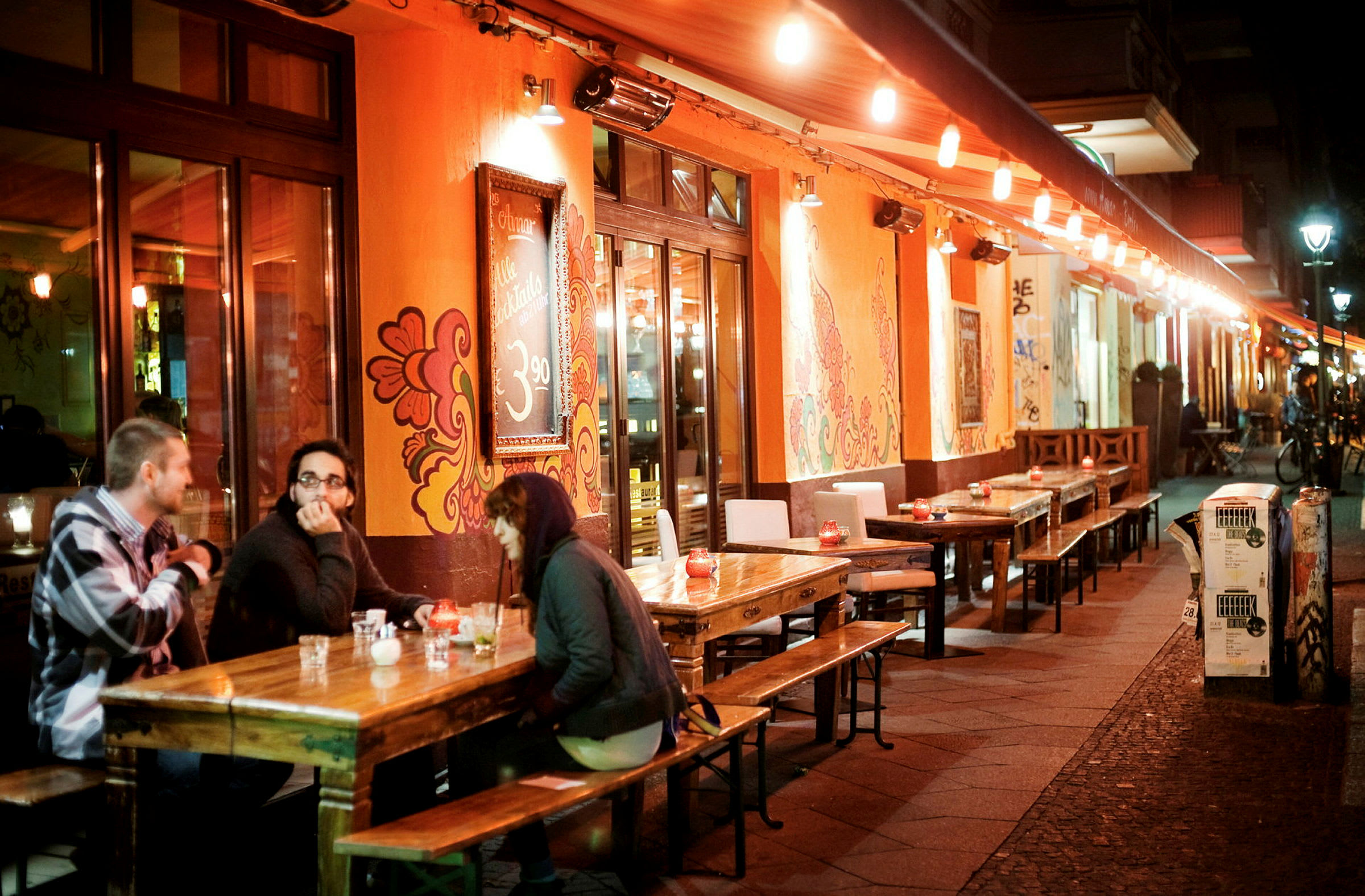 En kafé med uteservering opplyst av lys der folk sitter og prater. (AI-generert tekst)