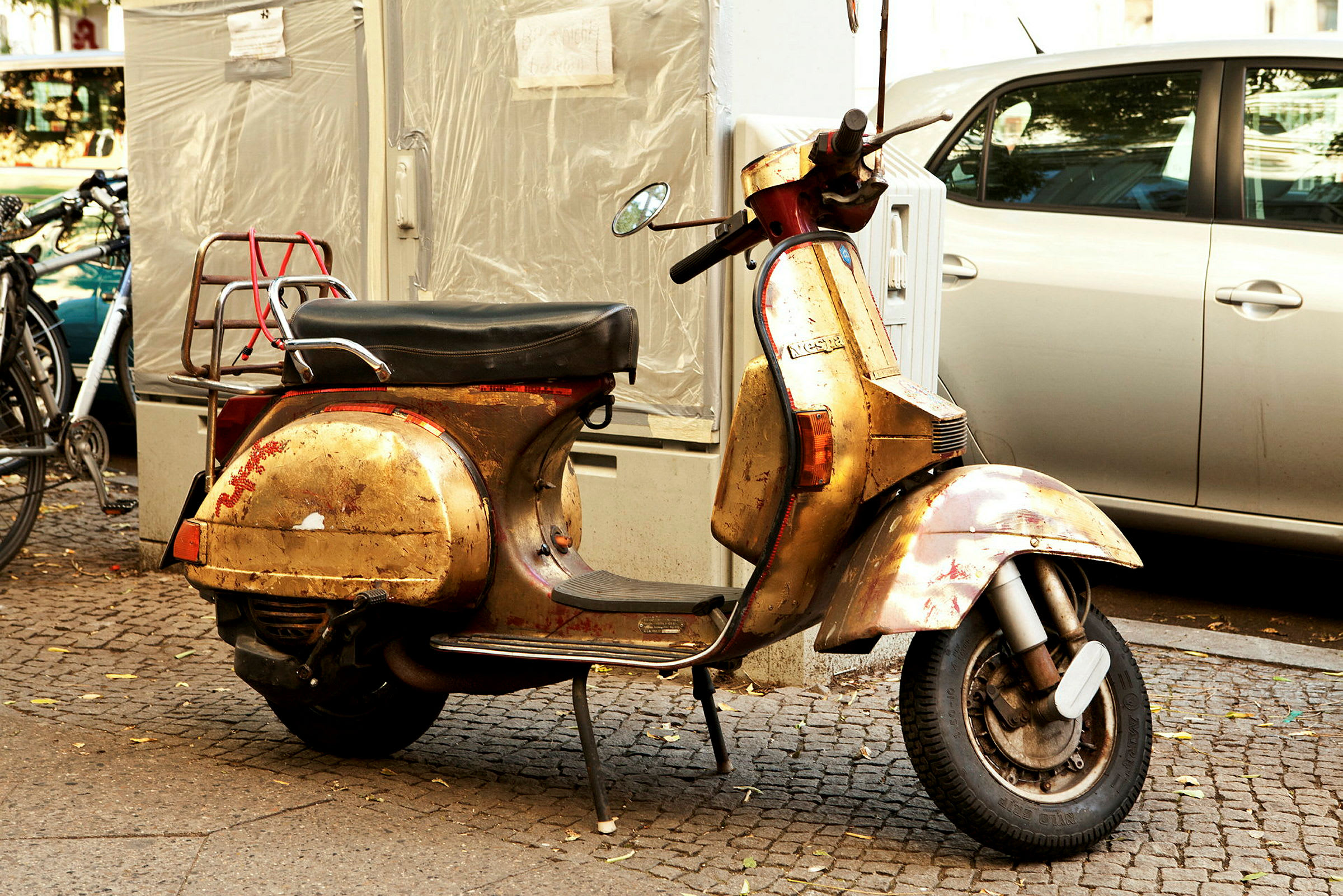 En gammel gullfarget scooter står parkert på en fortau ved siden av andre kjøretøy. (AI-generert tekst)