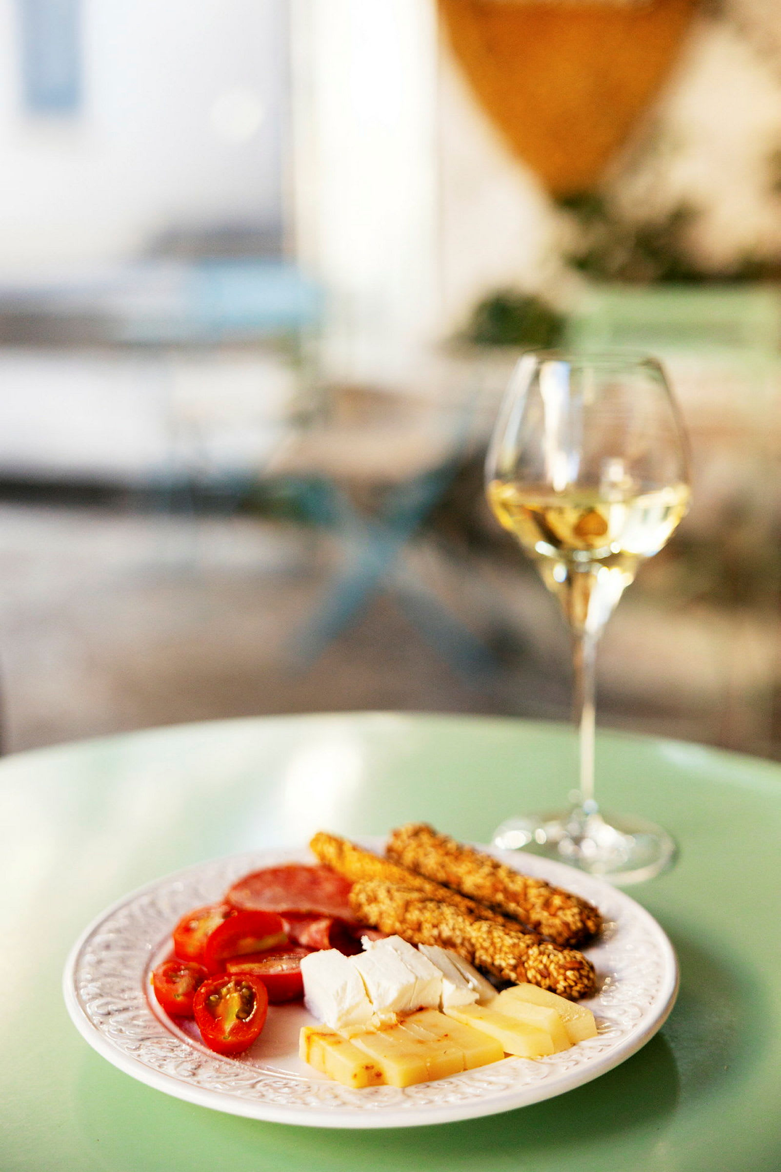 En tallerken med ost, brødpinner og cherrytomater, ved siden av et glass hvitvin, plassert på et grønt bord. (AI-generert tekst)