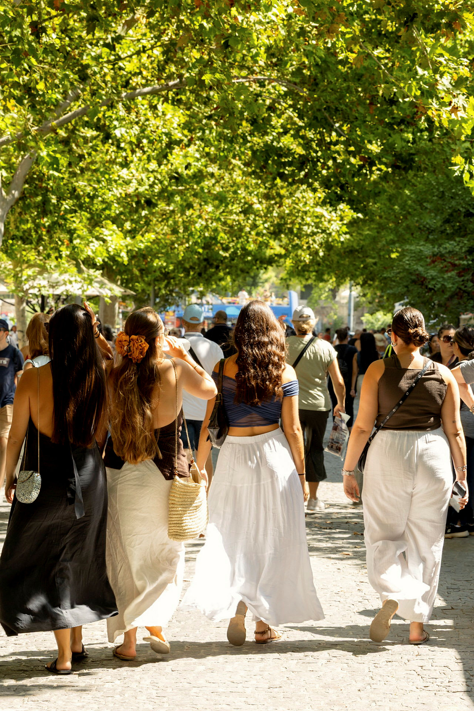 Fem personer går langs en skyggefull promenade med trær som omgir området. (AI-generert tekst)