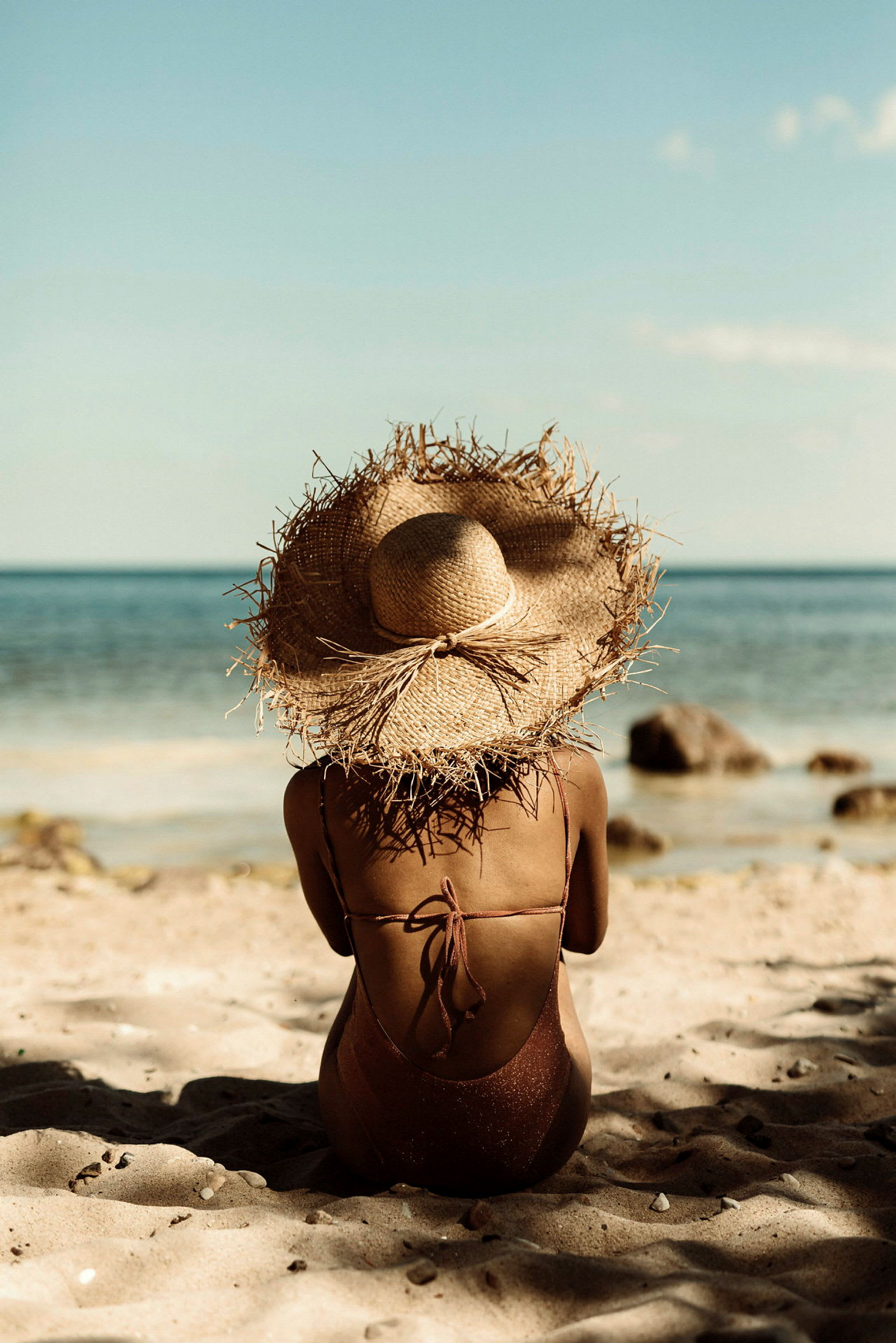 En person med solhatt sitter på stranden med havet i bakgrunnen. (AI-generert tekst)