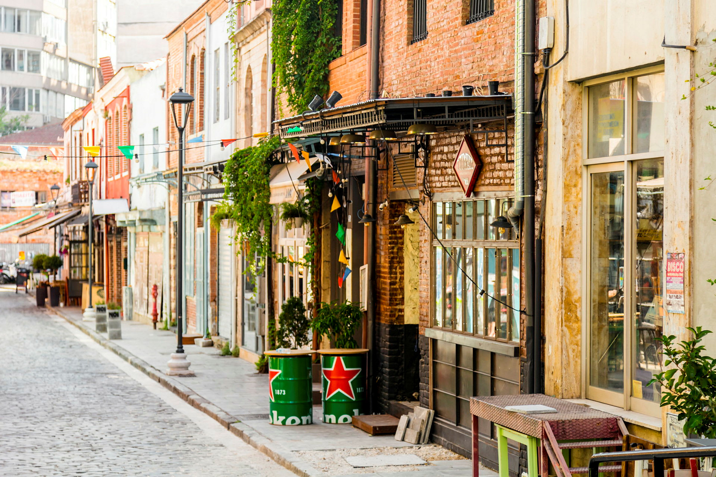 En gate med bygninger dekorert med fargerike flagg og tønner med Heineken-logoen. (AI-generert tekst)