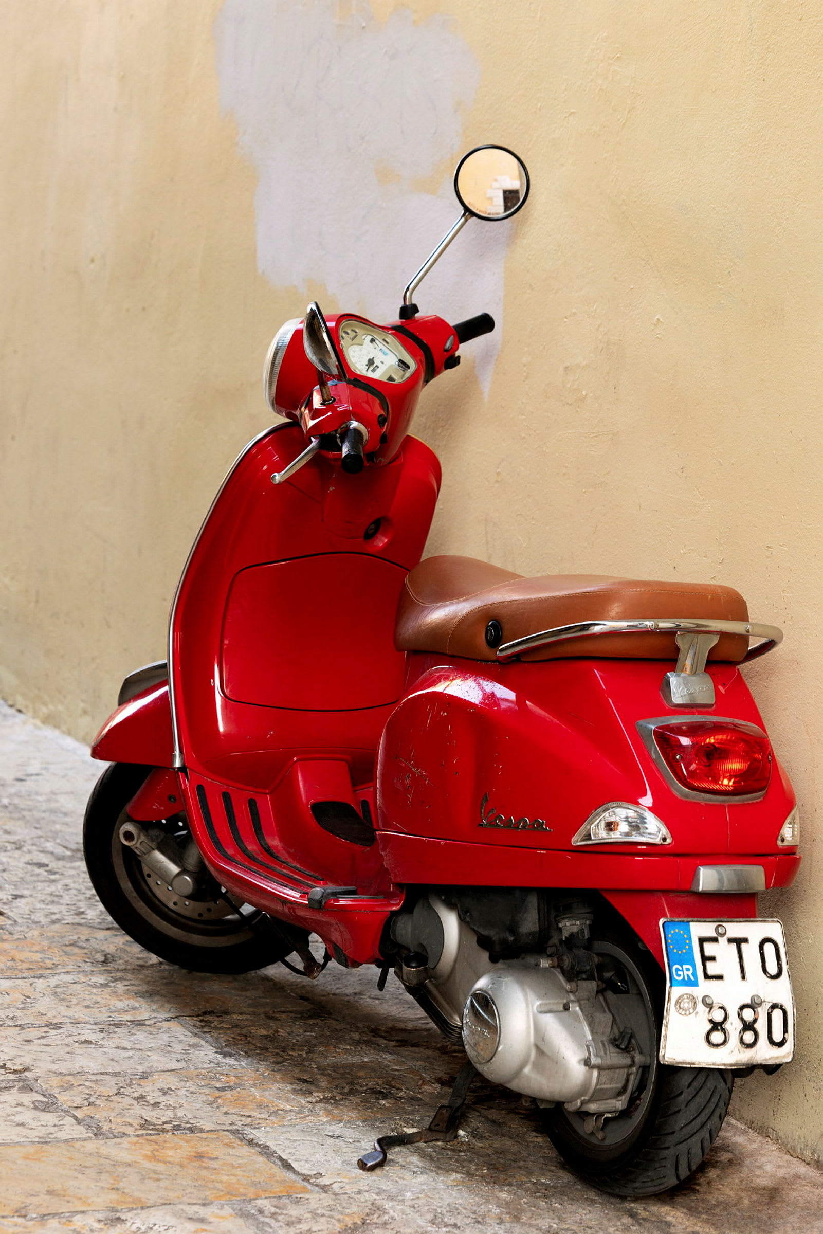 En rød scooter lener seg mot en beige vegg. (AI-generert tekst)