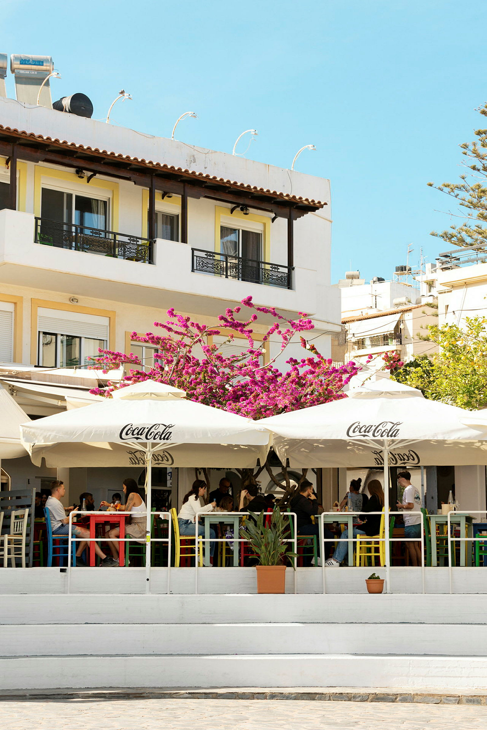 Utendørs kafé med parasoller og blomster foran en bygning. (AI-generert tekst)