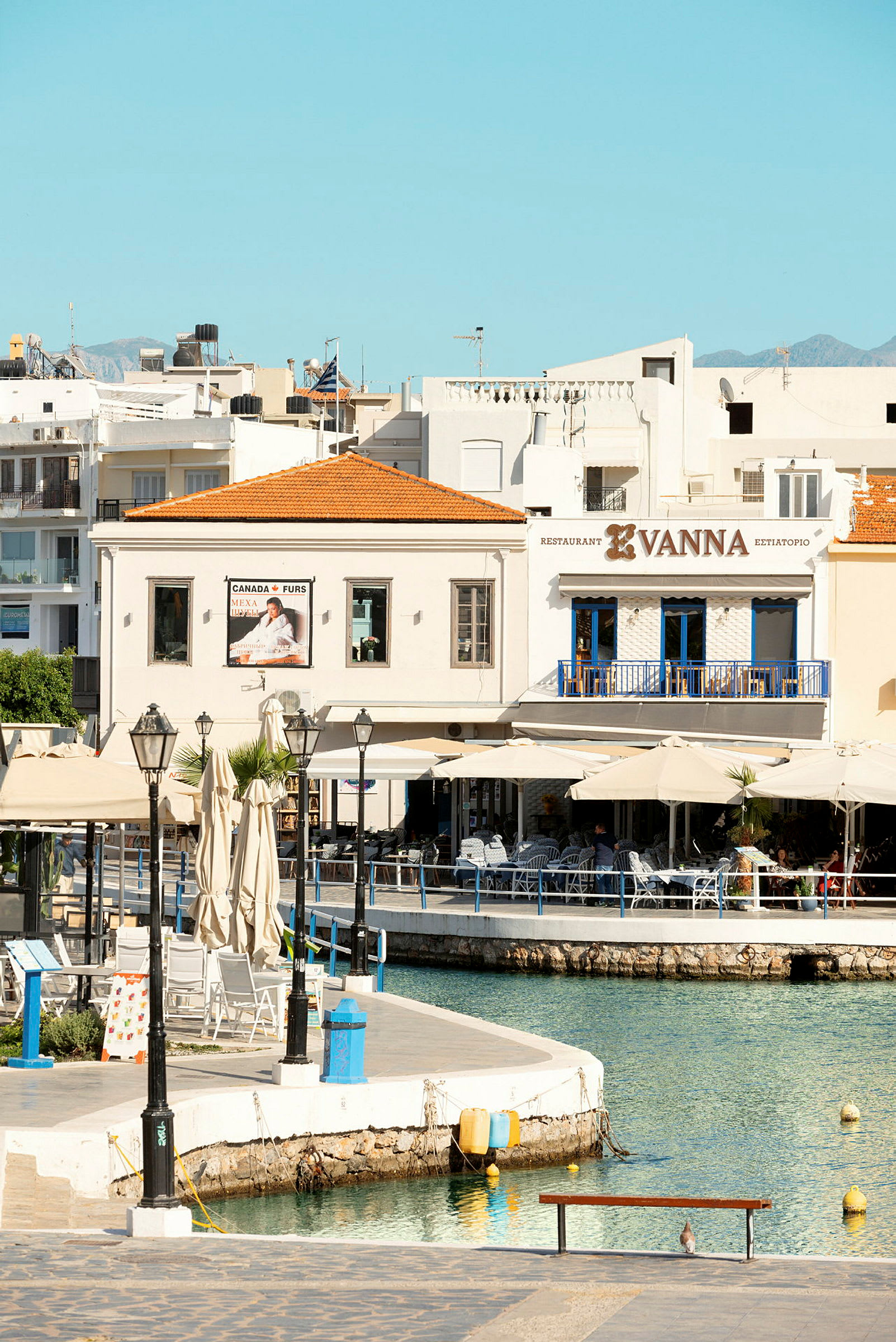 Utsikt over en liten havn med sitteplasser og restaurant Vanna. (AI-generert tekst)