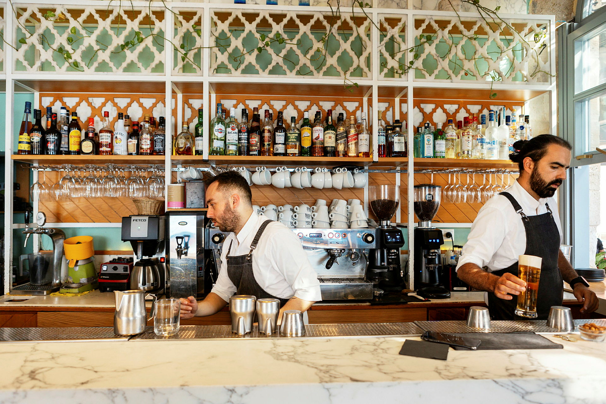 En bar med vitrineskap fylt med spritflasker, kaffekopper og glass. Kaffemaskiner står på bardisken. (AI-generert tekst)