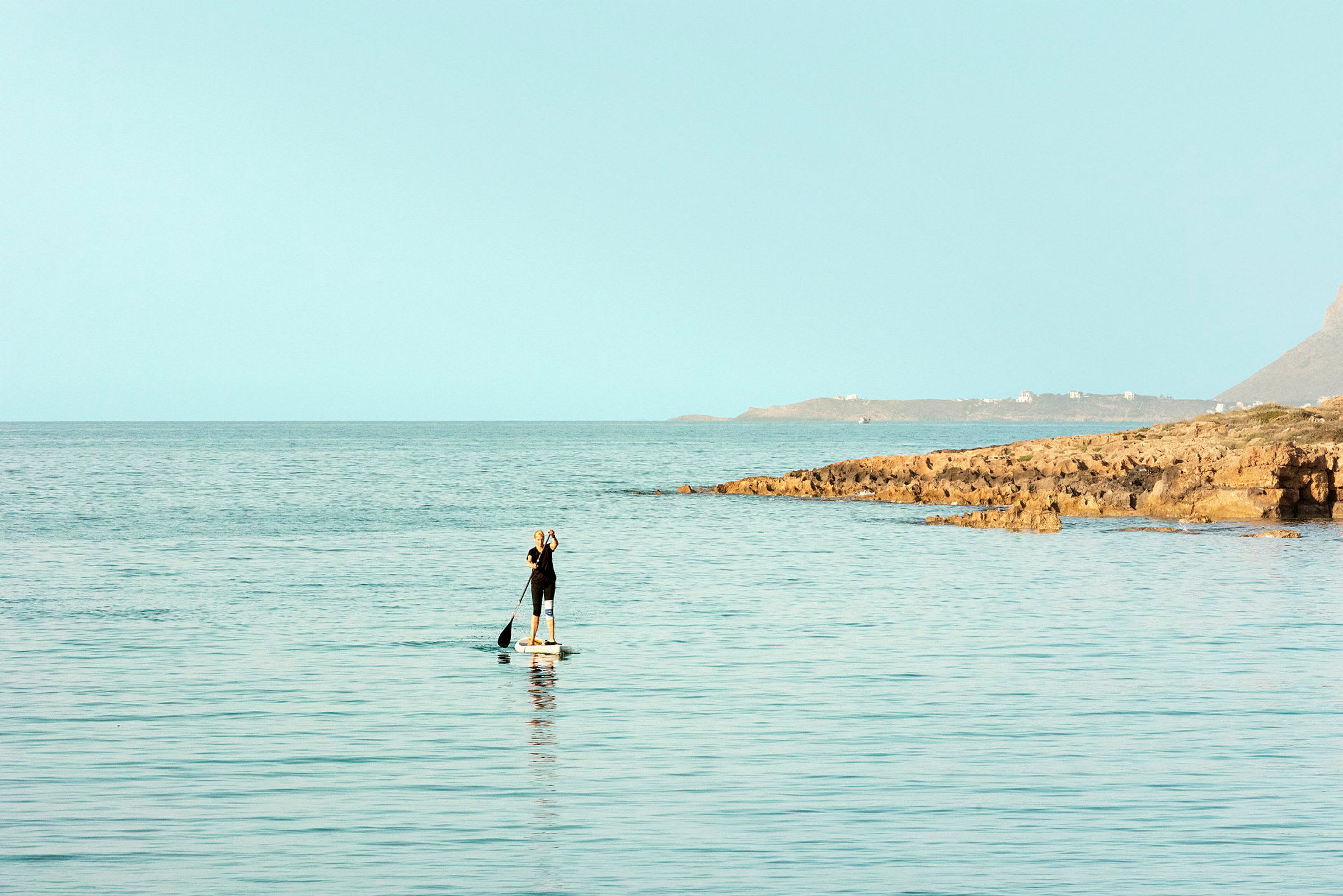 En person som padler på et paddleboard i sjøen nær en steinete kyst. (AI-generert tekst)