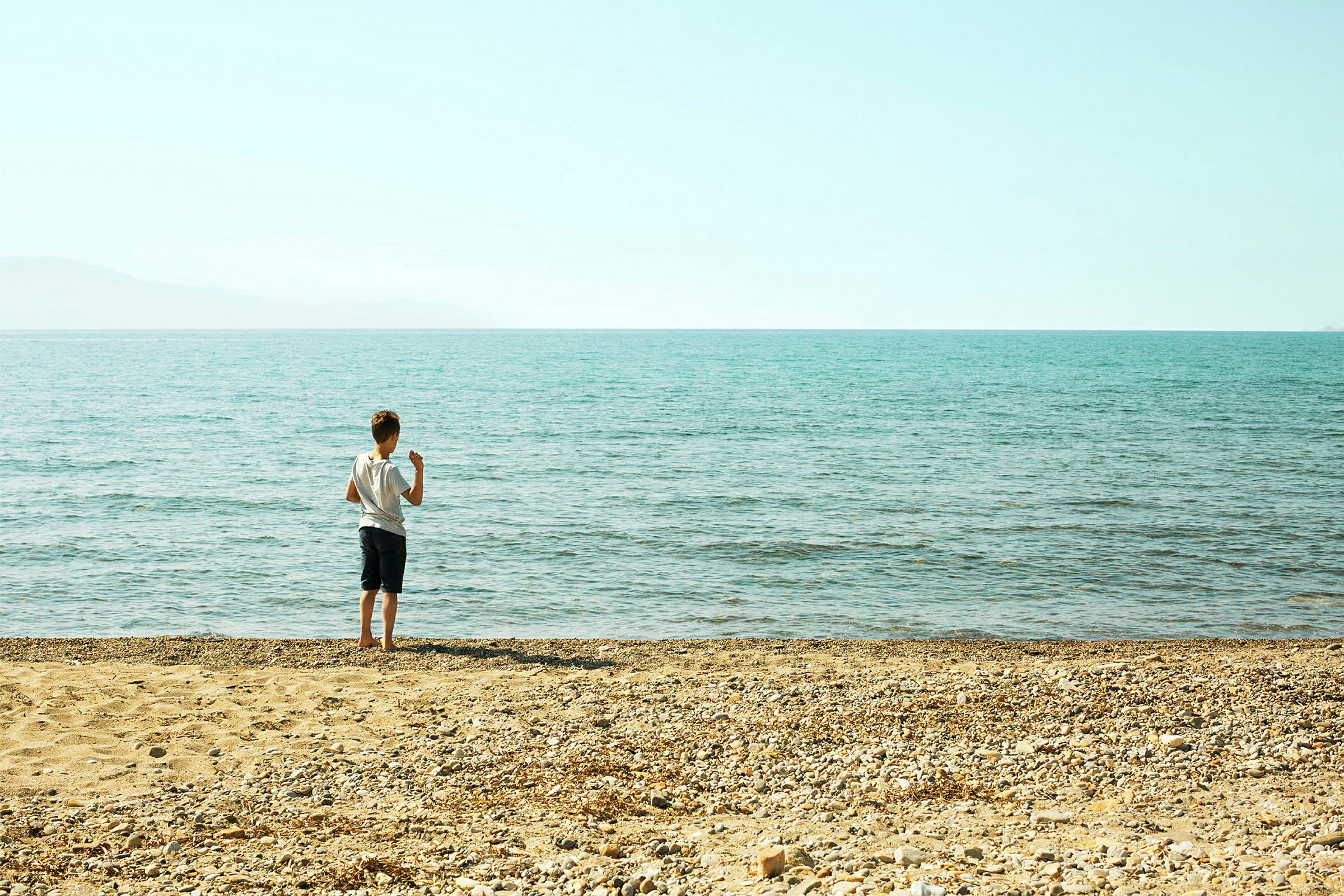 Et barn står på en steinete strand og ser ut over havet. (AI-generert tekst)