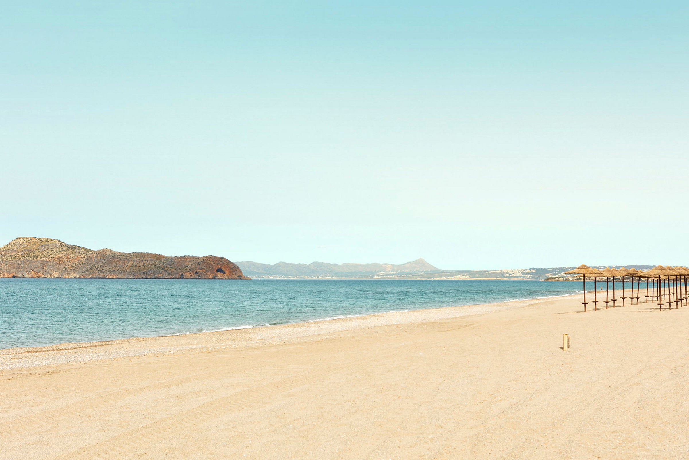 Strand med parasoller og hav i bakgrunnen. (AI-generert tekst)