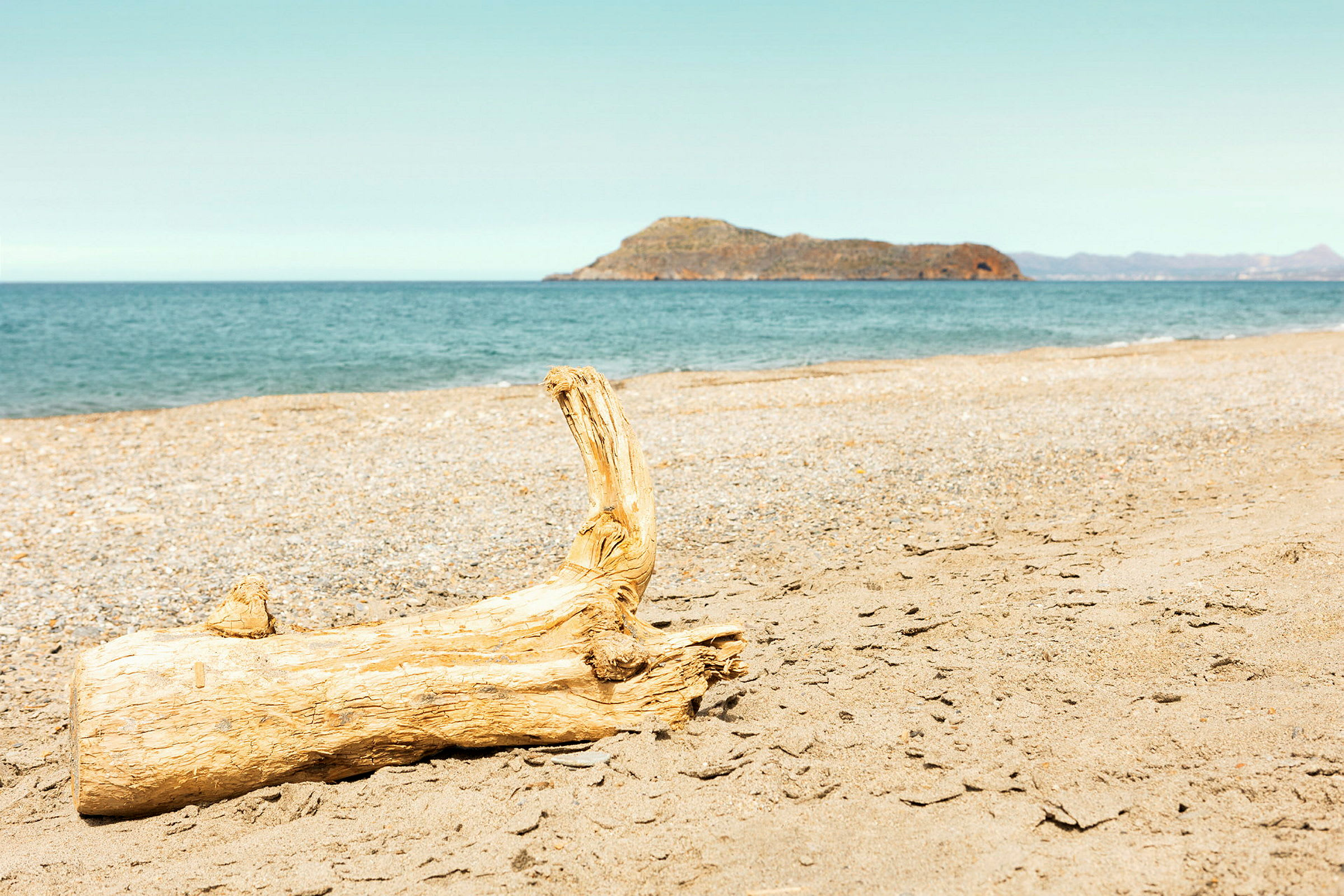 Et trestykke ligger på stranden med havet og en fjellrik øy i bakgrunnen. (AI-generert tekst)