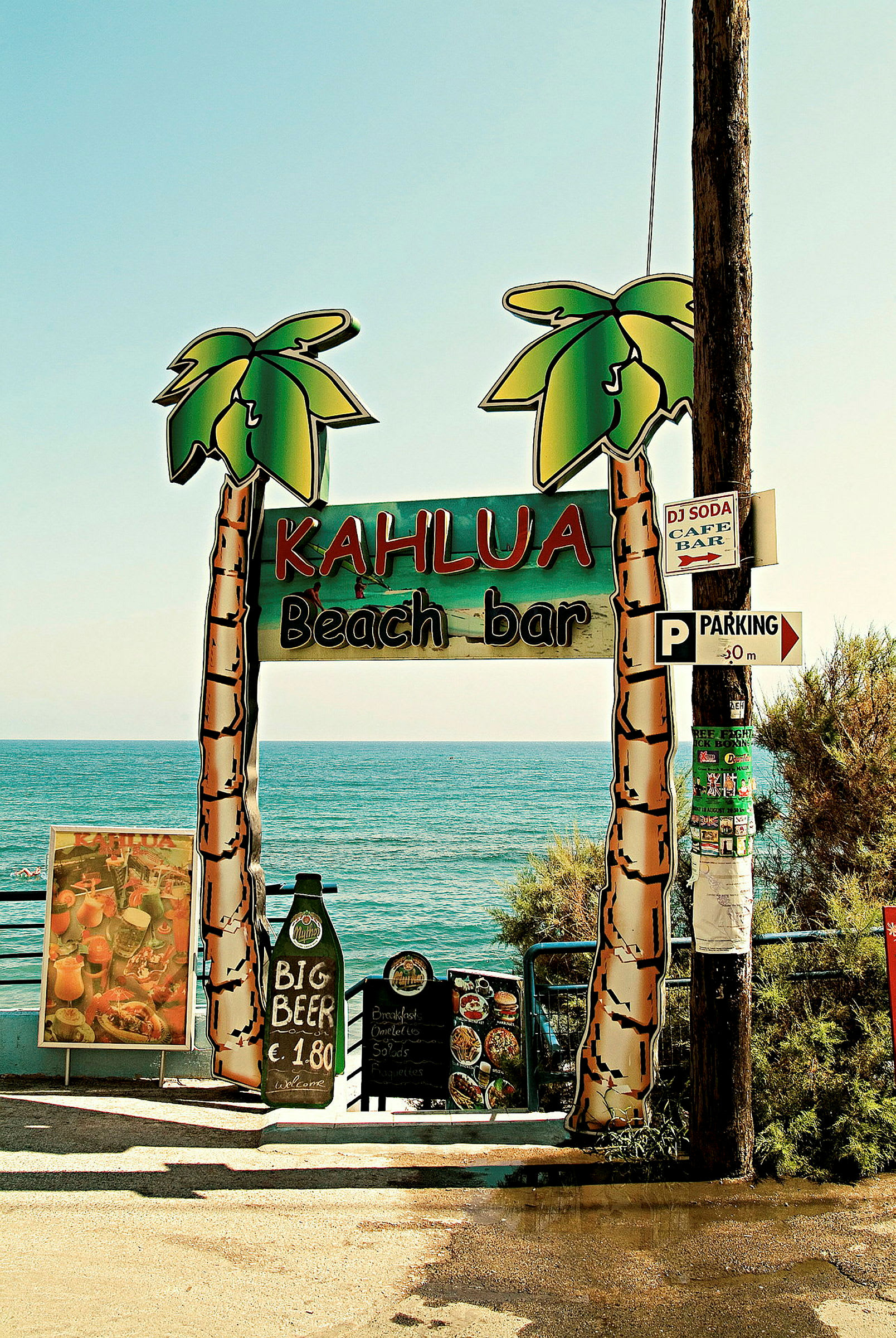 Bilde av et skilt med teksten 'Kahlua Beach Bar' foran havet. (AI-generert tekst)