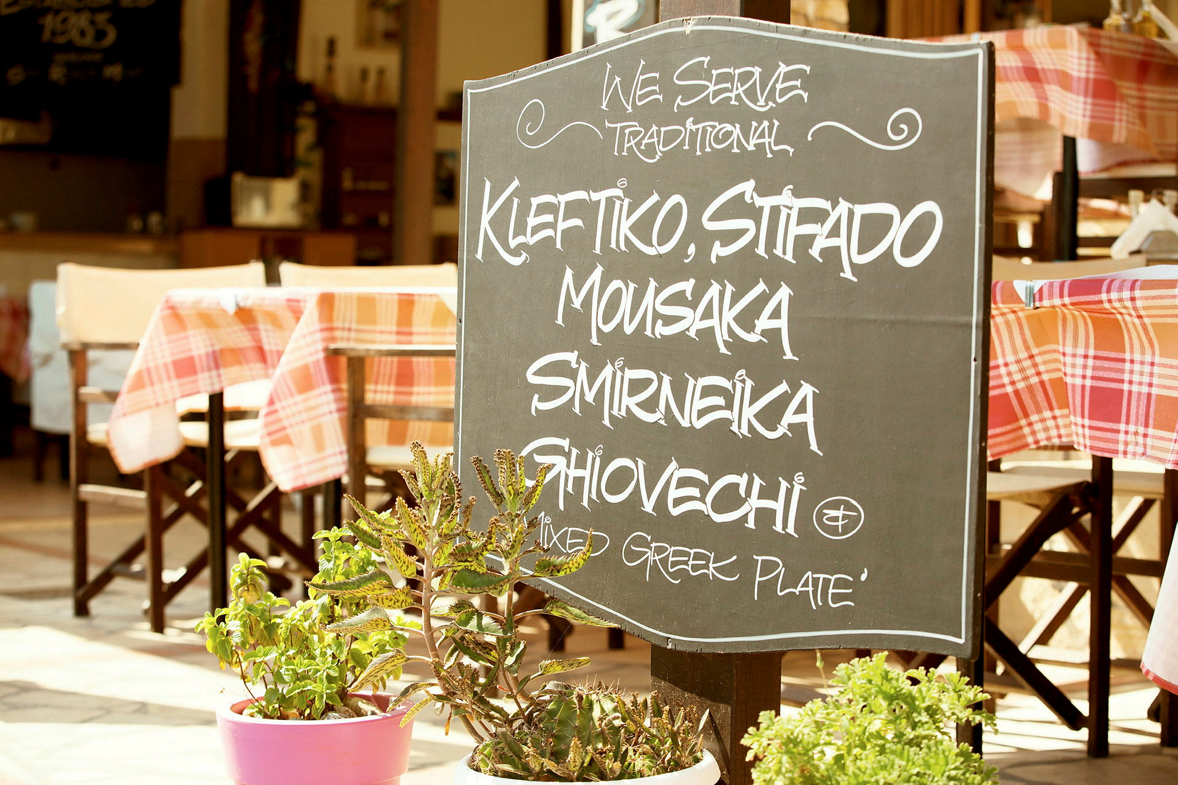 Et skilt utenfor en restaurant med tekst som oppgir tradisjonelle greske retter. (AI-generert tekst)