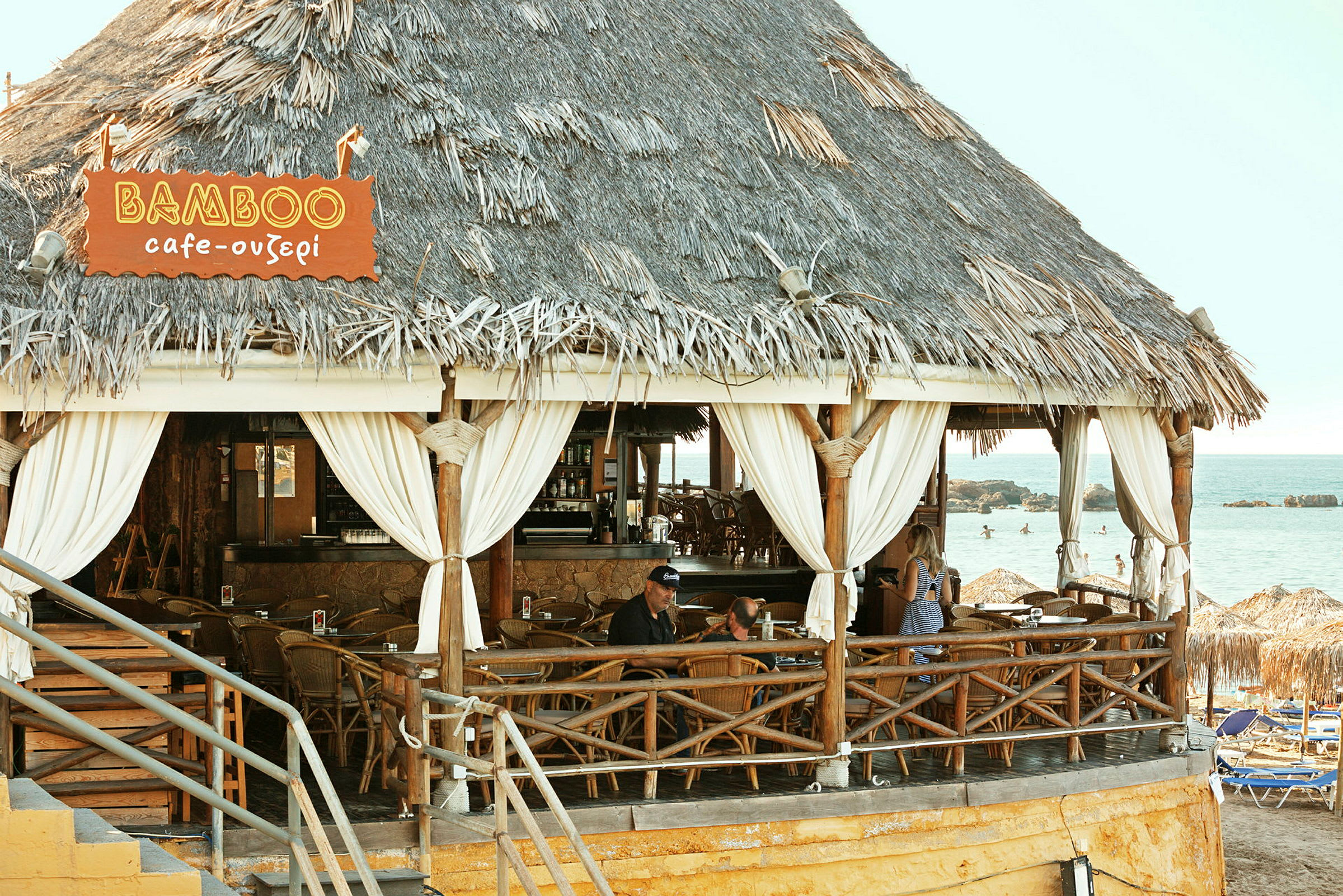 En strandbar med stråtak og treinteriør ved havet. (AI-generert tekst)