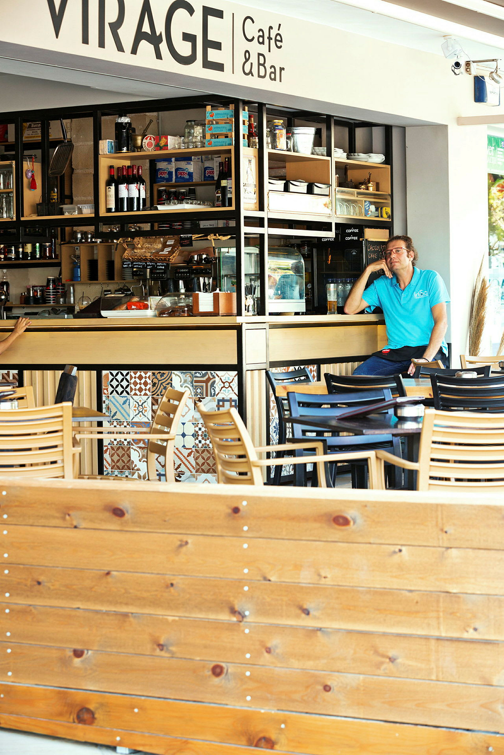 Uteservering ved en kafé med stoler og bord samt en synlig del av interiøret og hyller med produkter. (AI-generert tekst)