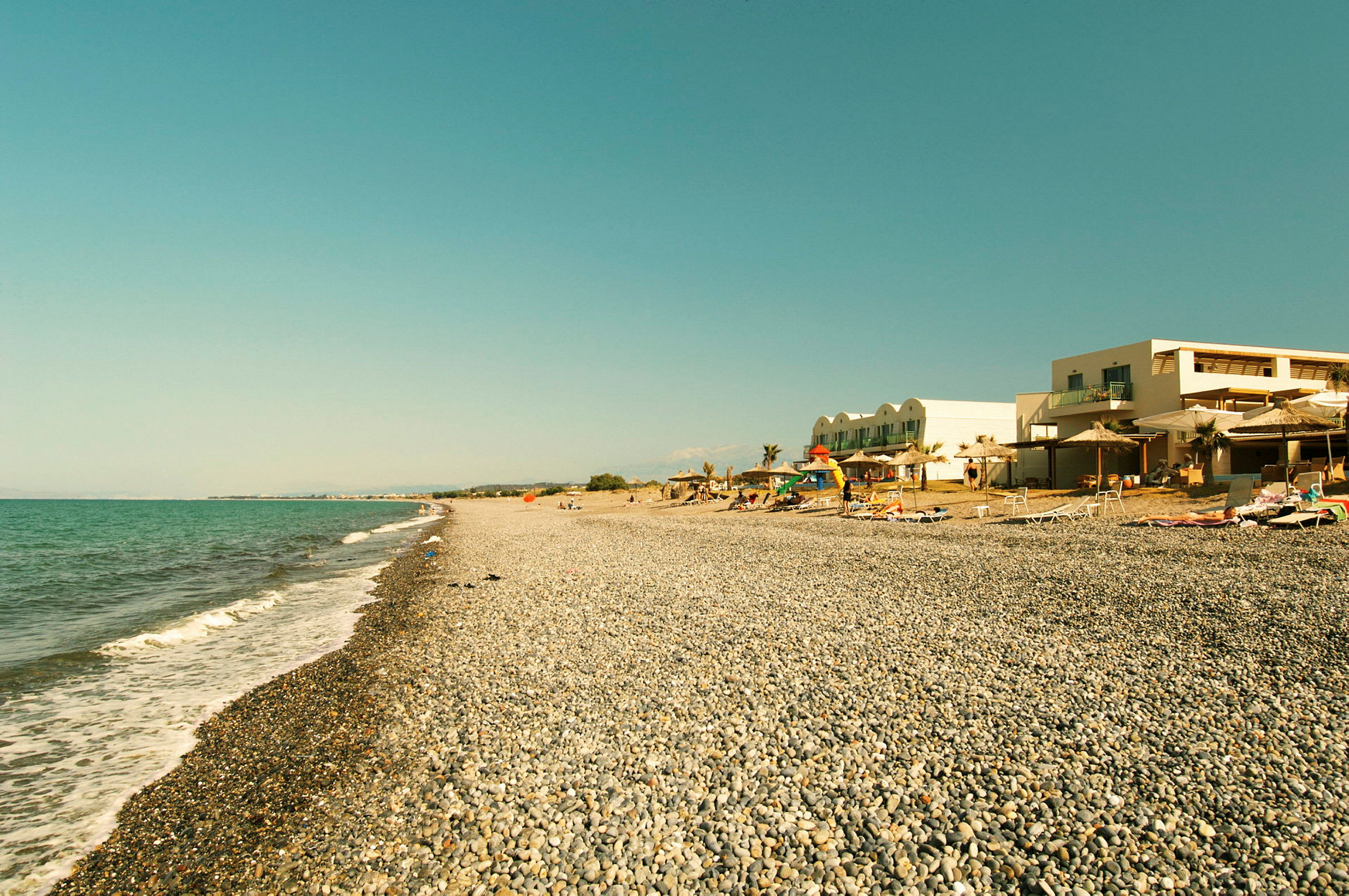 Strand med runde steiner og hotellbygning i bakgrunnen. (AI-generert tekst)
