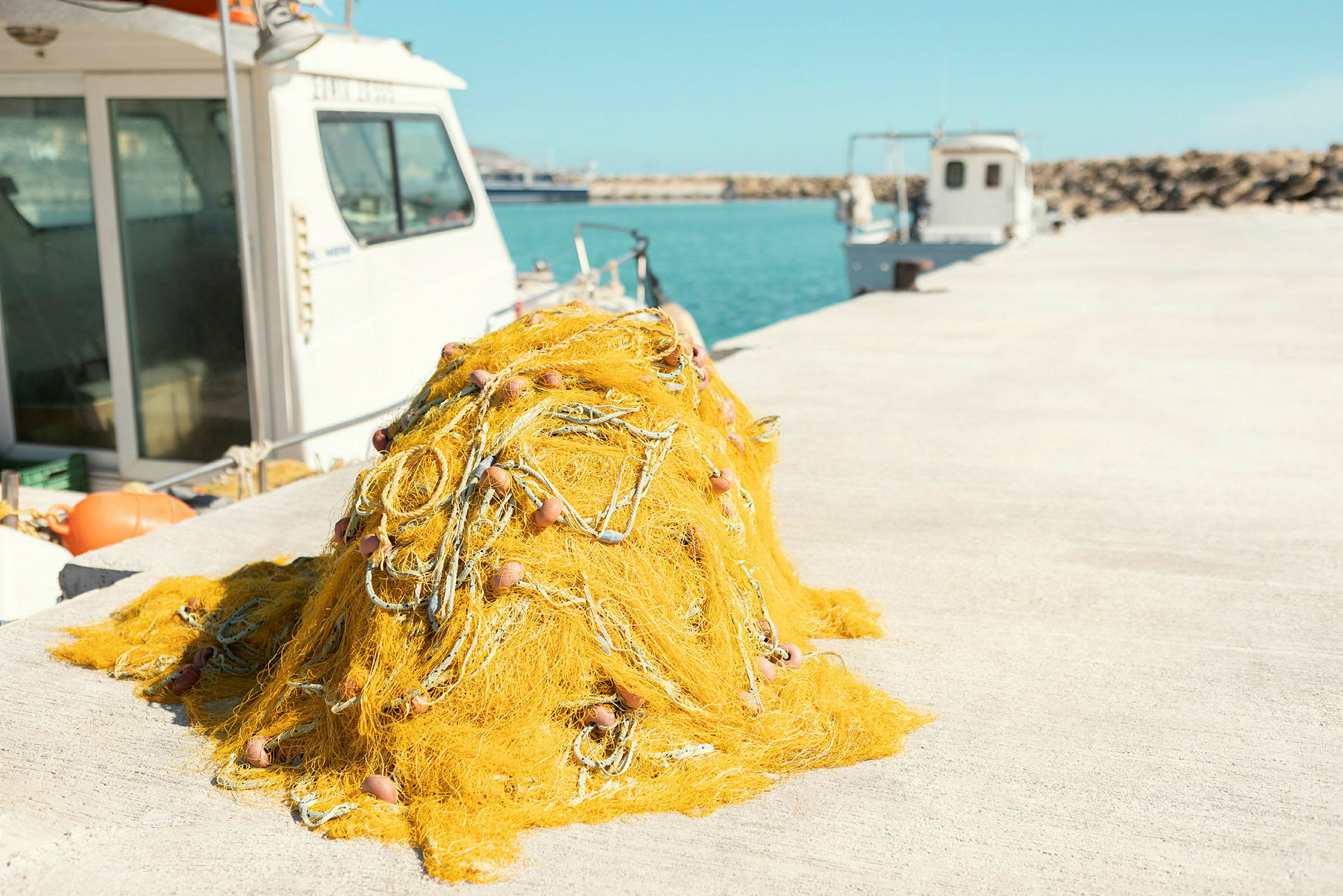 En haug med gul fiskegarn ligger på en kai, med båter og havet i bakgrunnen. (AI-generert tekst)