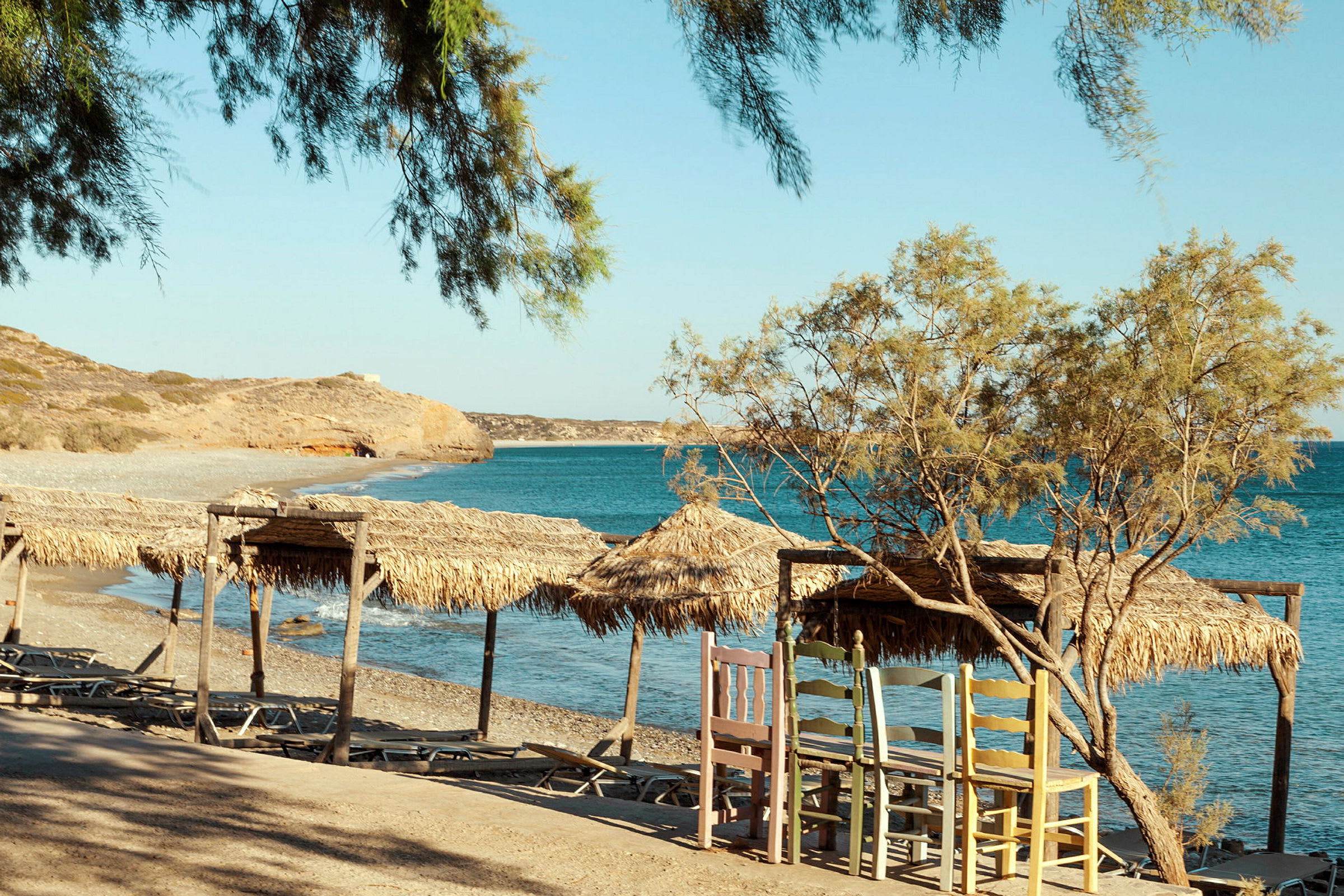 En strand med parasoller av halm nær klart blått vann. (AI-generert tekst)