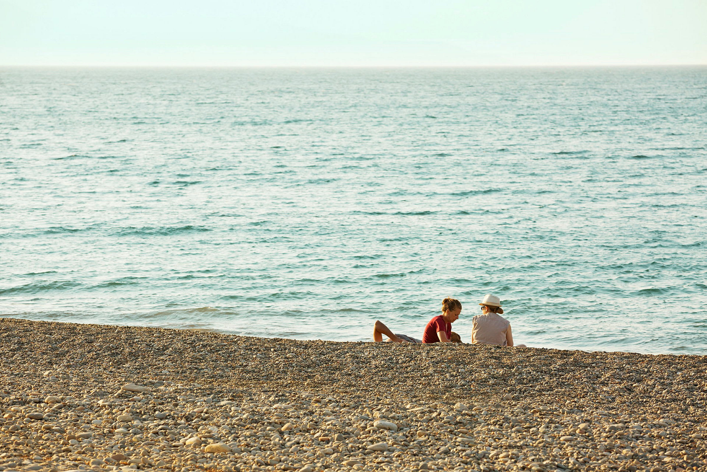 To personer sitter på en steinstrand ved havet. (AI-generert tekst)