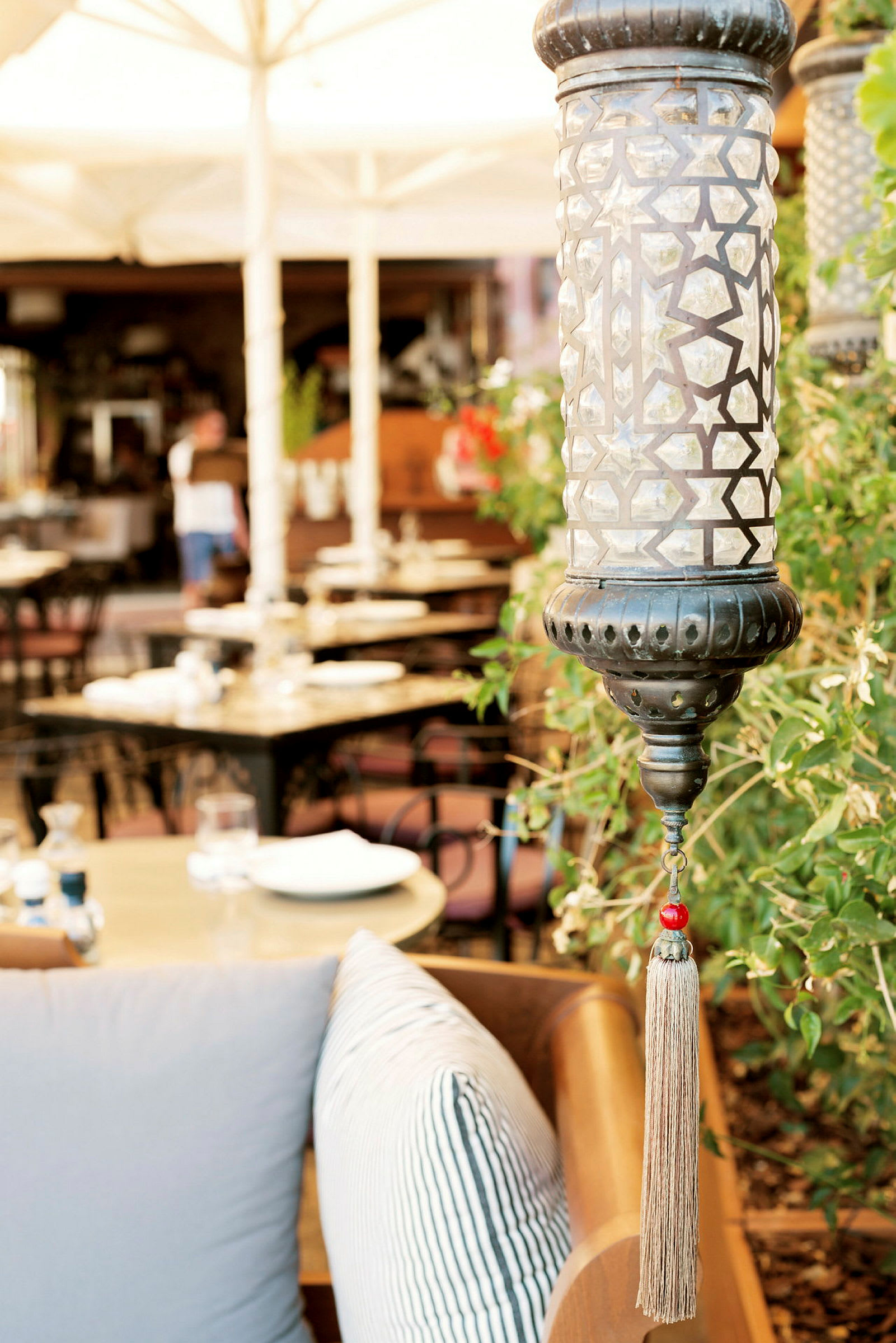 Nærbilde av en dekorativ lampe med geometrisk mønster og frynser, med en restaurant i bakgrunnen. (AI-generert tekst)