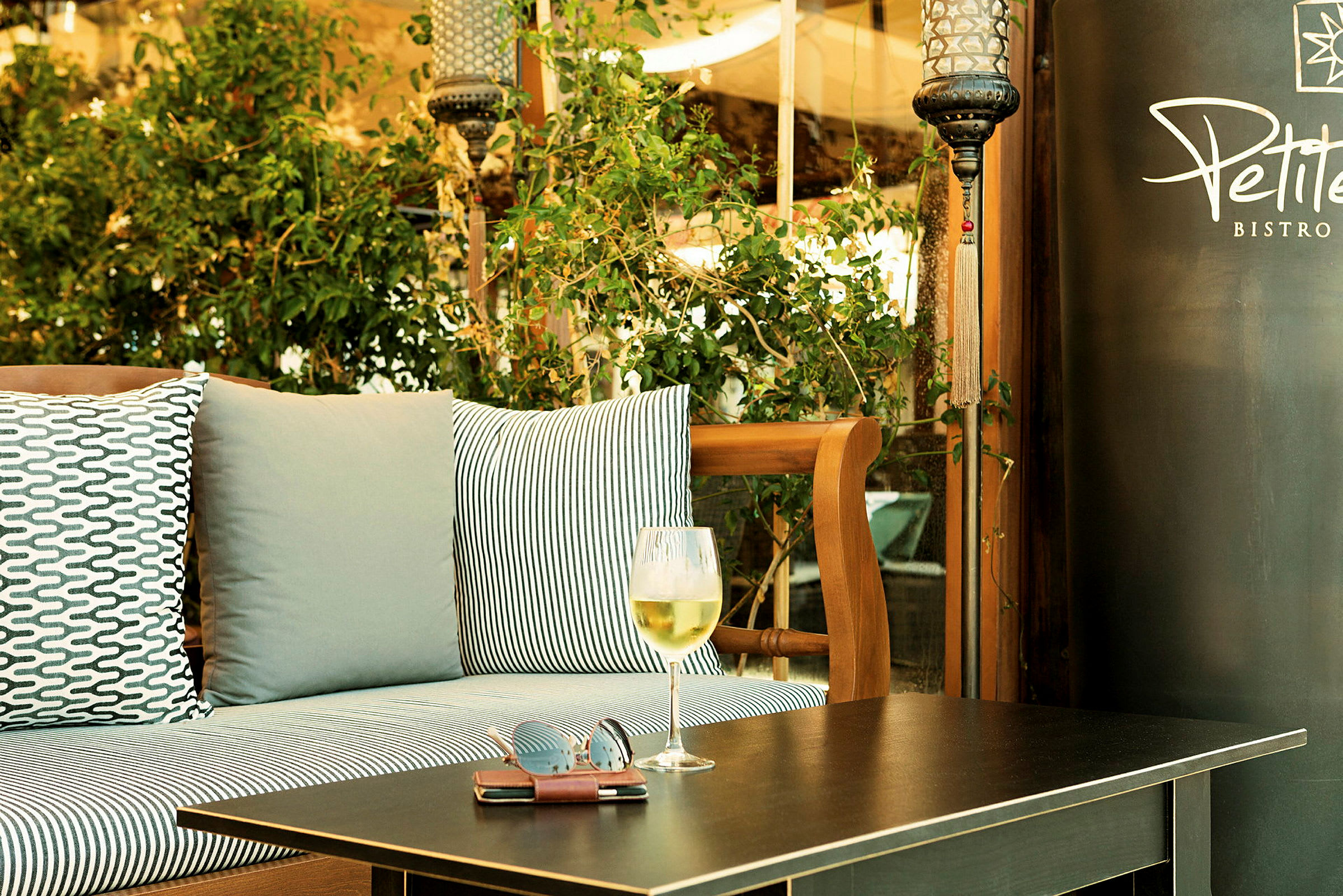 Utendørs miljø med sitteplass, puter og et bord med et glass vin og solbriller. (AI-generert tekst)