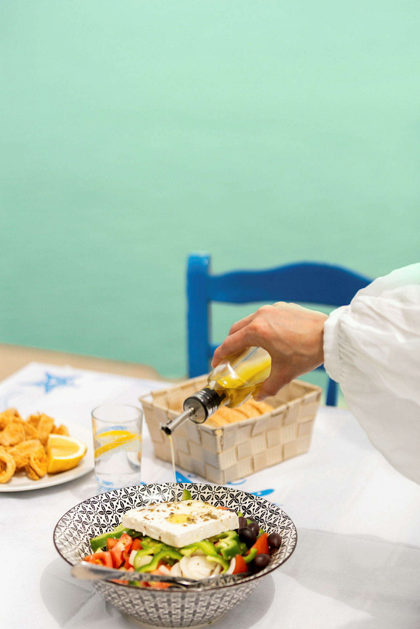 En hånd heller olivenolje over en gresk salat på et bord. (AI-generert tekst)