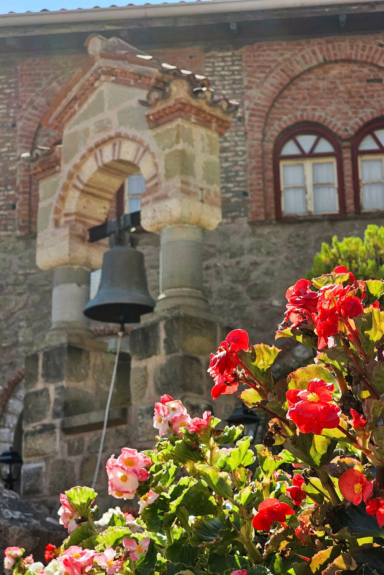Bilde av en kirkebygning med en klokke i forgrunnen og røde blomster i fokus. (AI-generert tekst)
