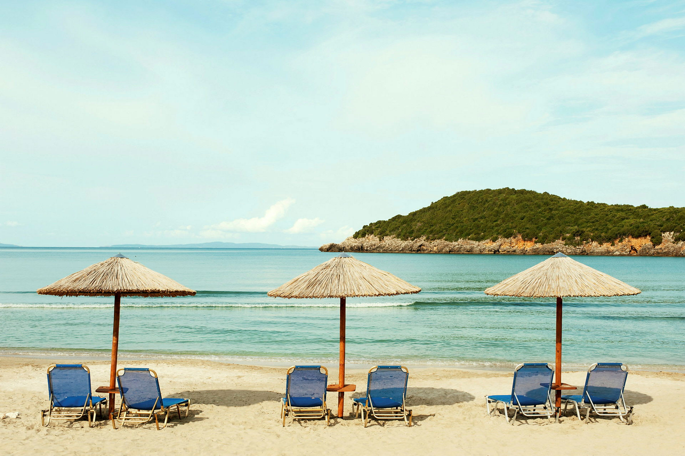 Solstoler med parasoller på en sandstrand ved havet. (AI-generert tekst)