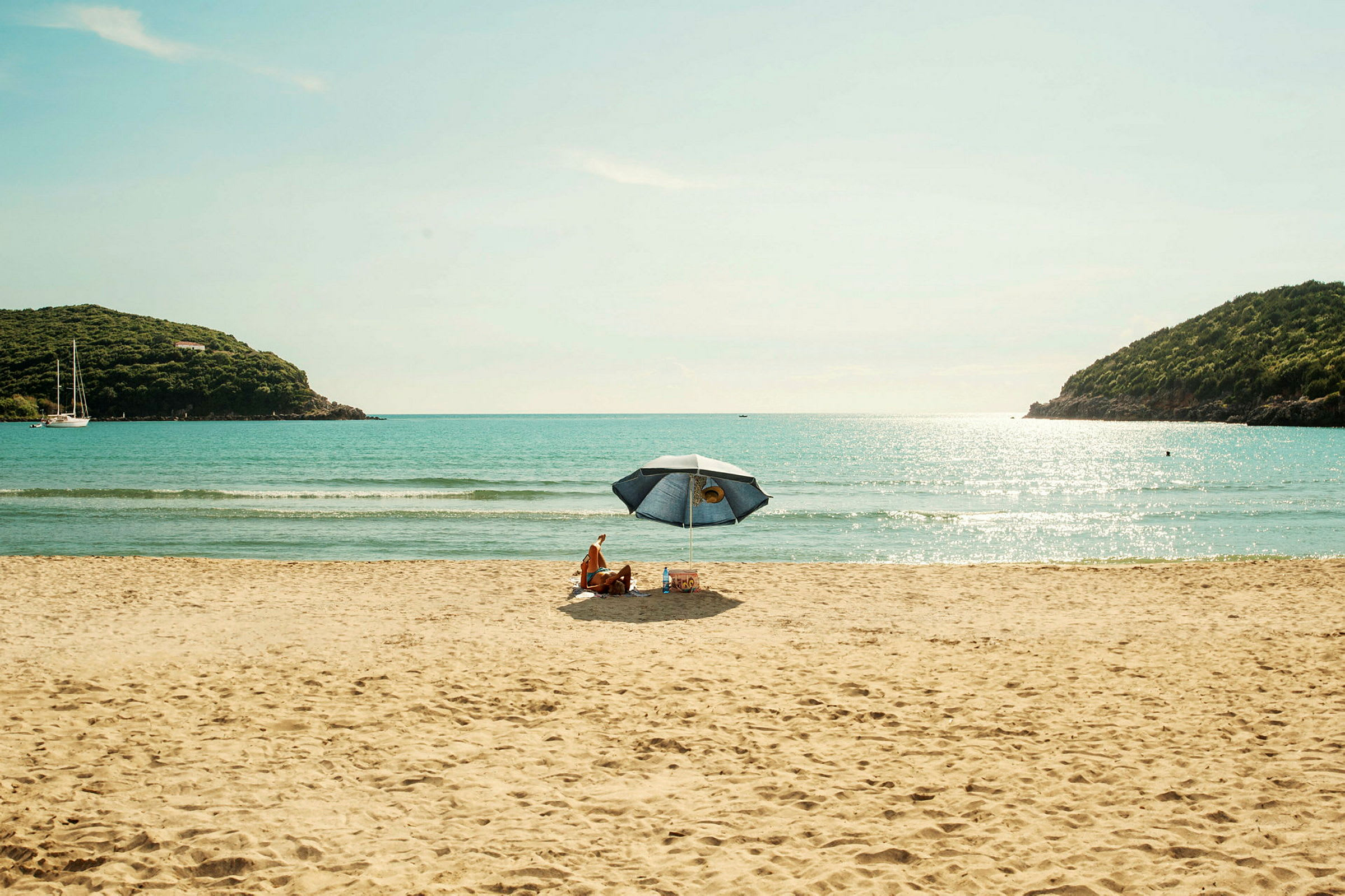 Personer sitter under en parasoll på en sandstrand med havet i bakgrunnen. (AI-generert tekst)