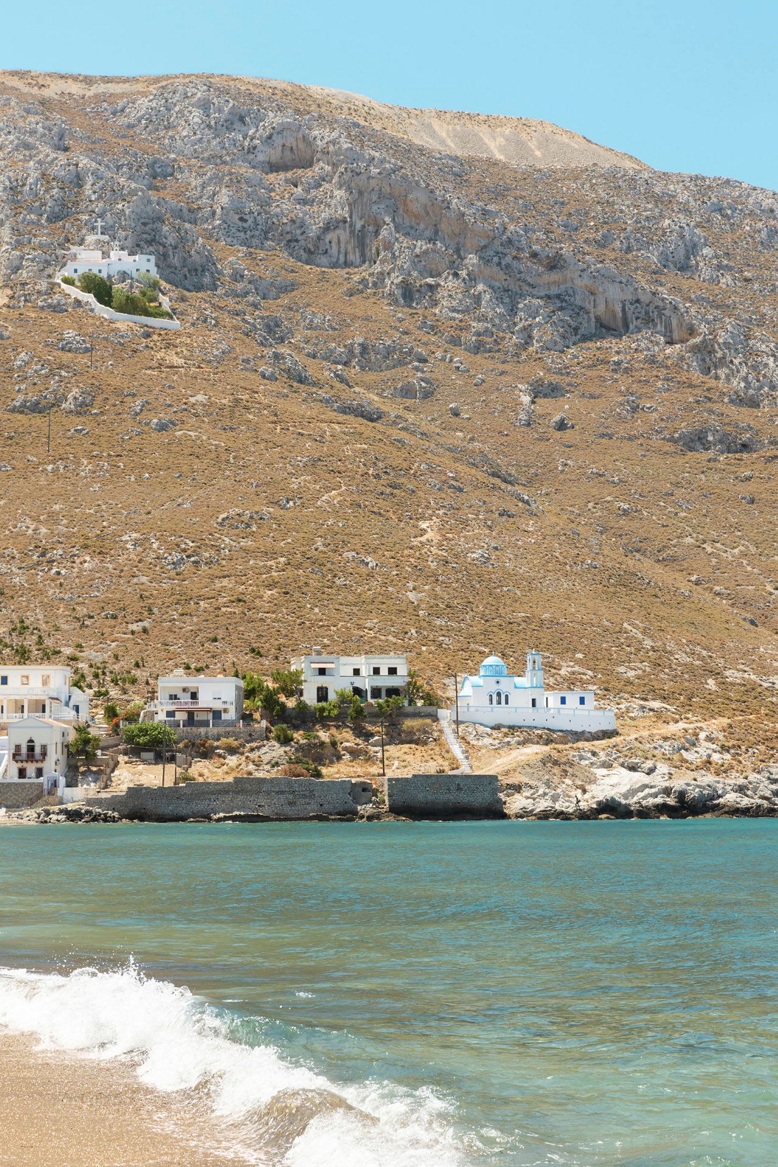 Strand med hav, bygninger og fjellbakke i bakgrunnen. (AI-generert tekst)