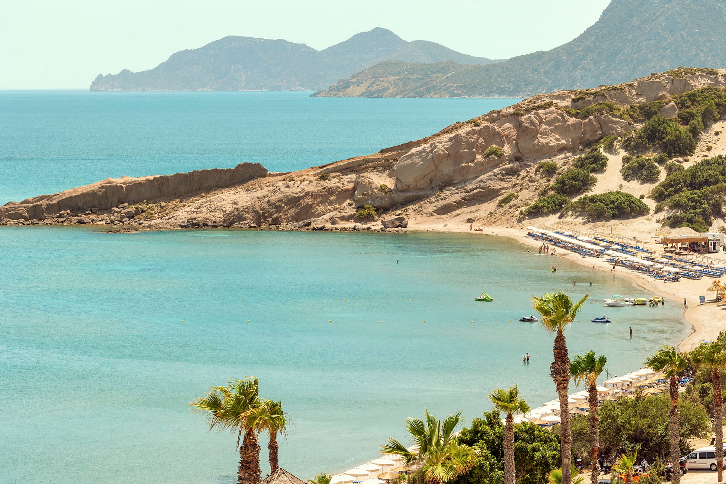 Strand med parasoller og solsenger ved en bukt med klart vann, omgitt av klipper og vegetasjon. (AI-generert tekst)