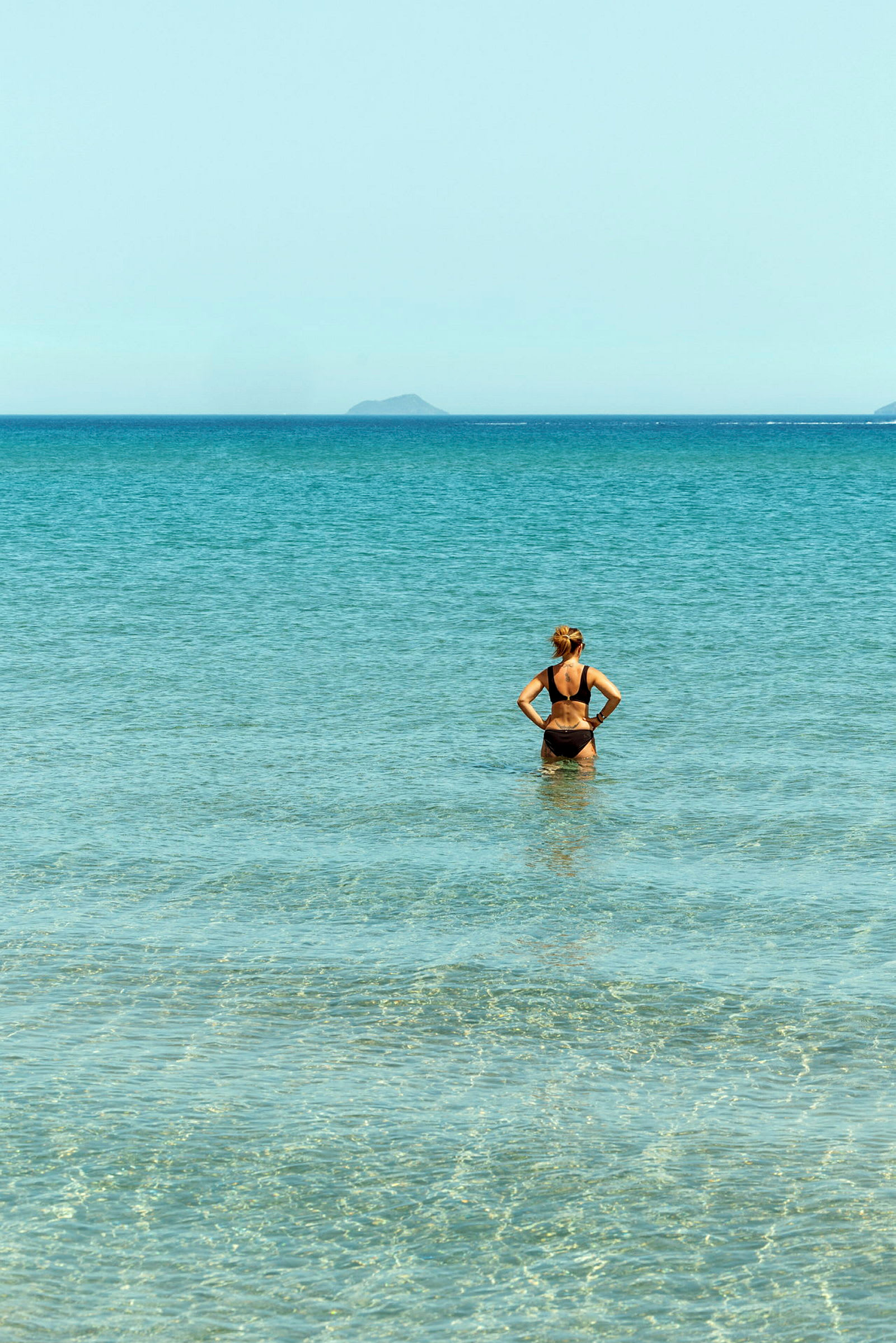 En person står i klart vann og ser ut mot havet. (AI-generert tekst)