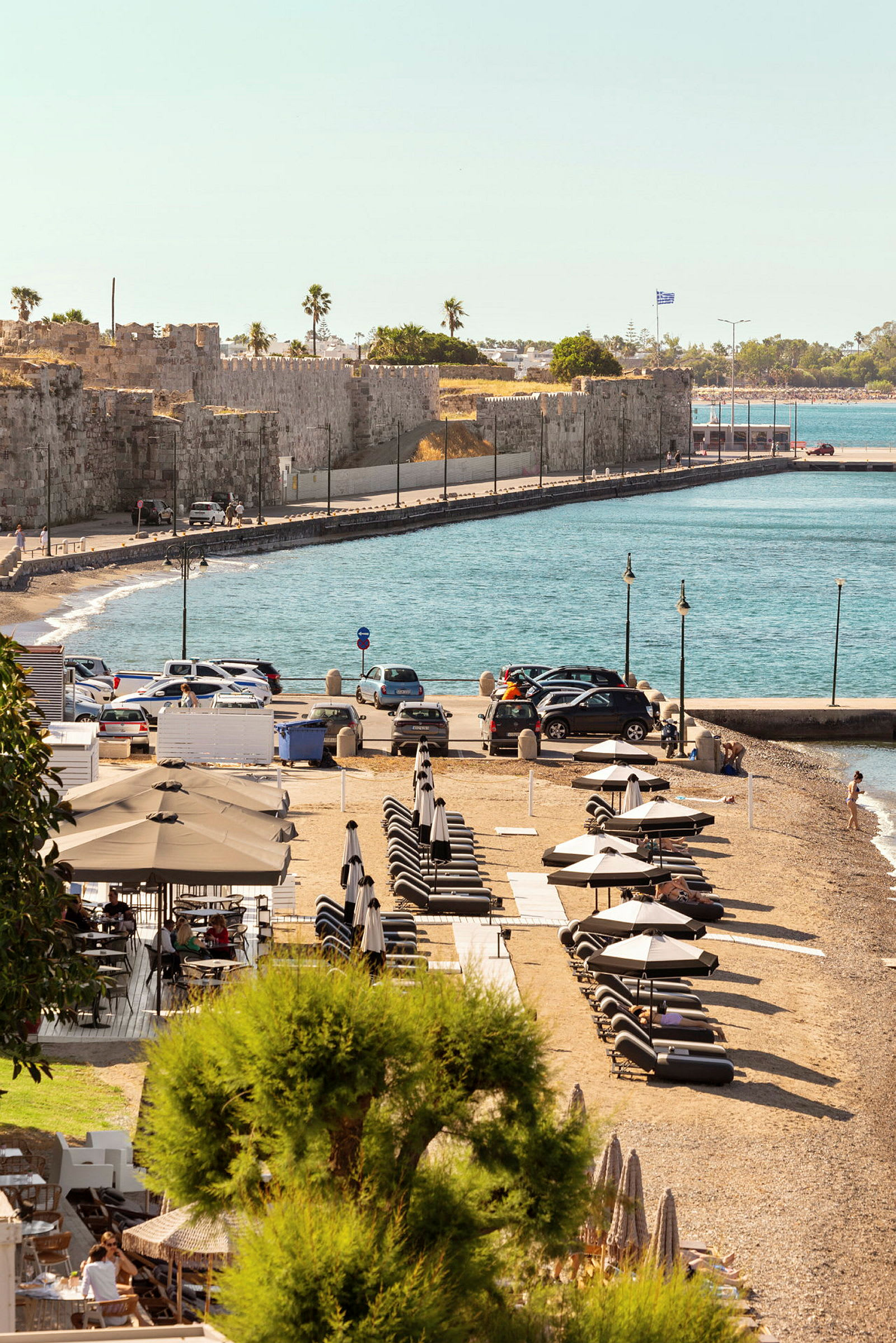 Strand med solsenger og parasoller nær klippevegger og blått hav. (AI-generert tekst)