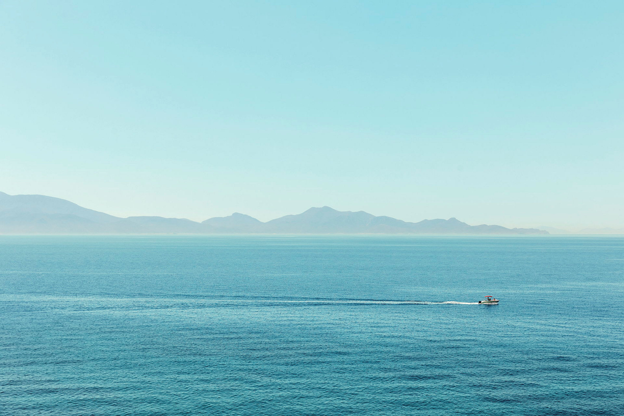 En båt på det åpne havet med fjell i bakgrunnen. (AI-generert tekst)
