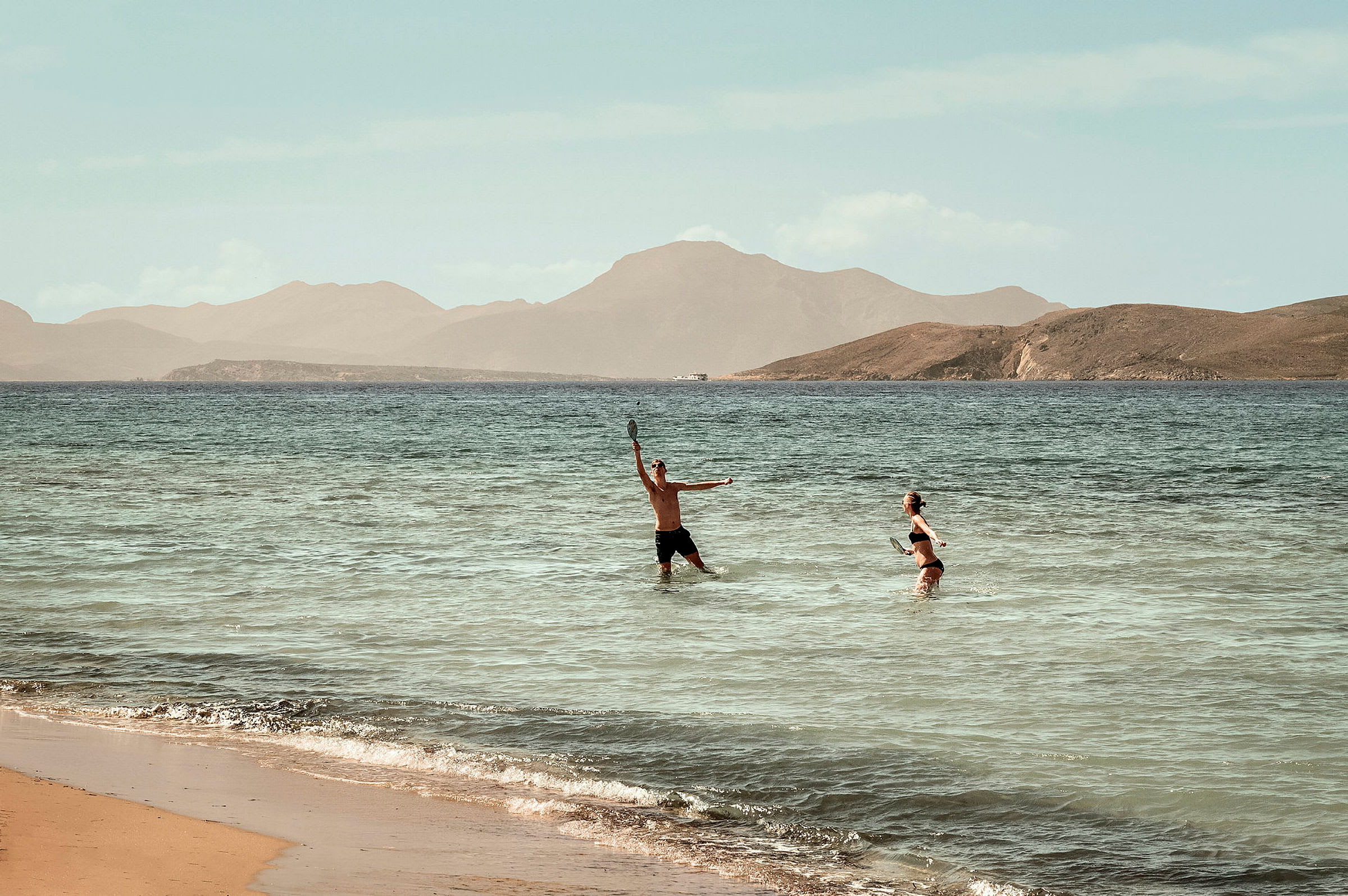 To personer spiller strandtennis i vannet ved en strand. (AI-generert tekst)