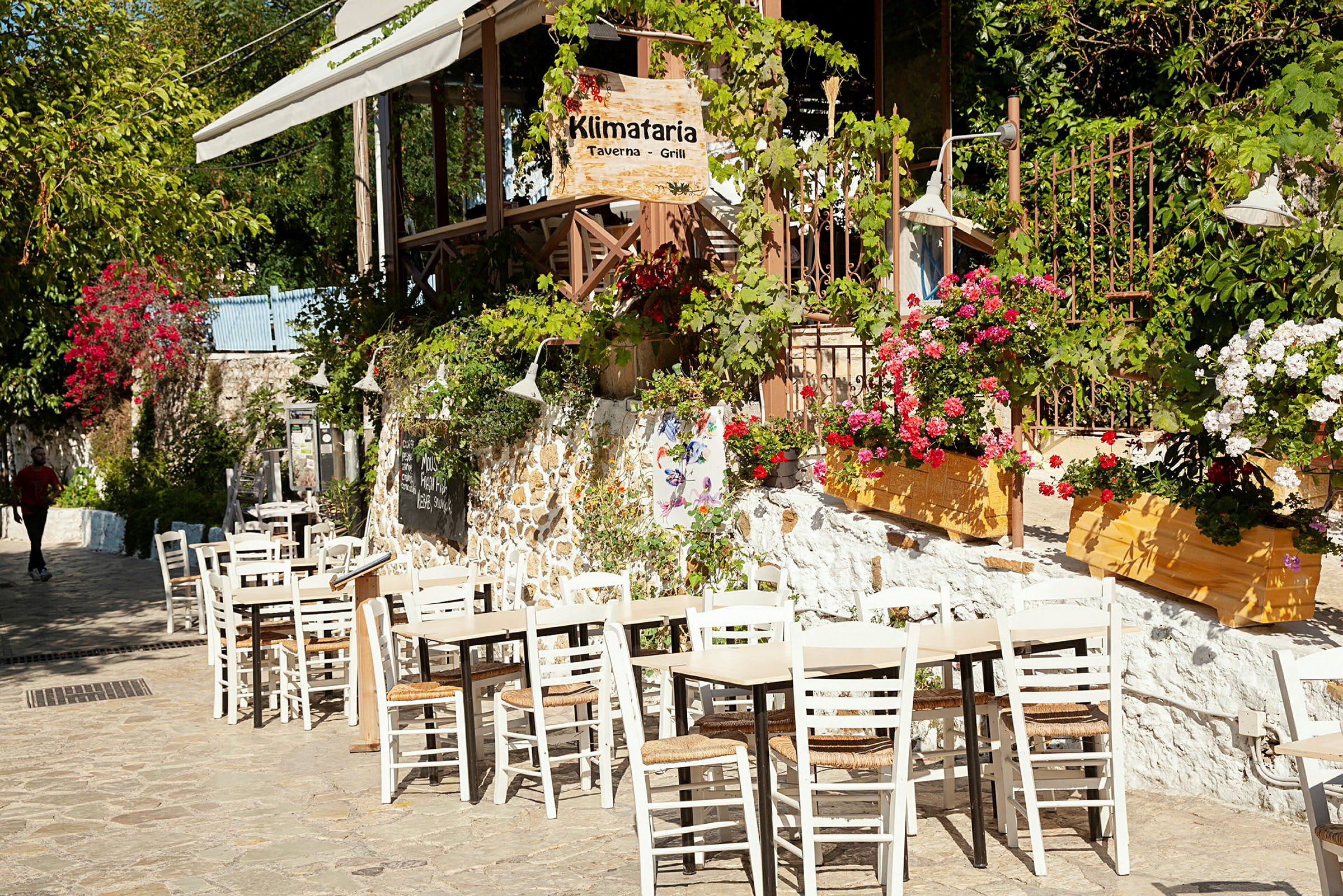 Uteservering ved en taverna, omgitt av blomstrende planter. (AI-generert tekst)