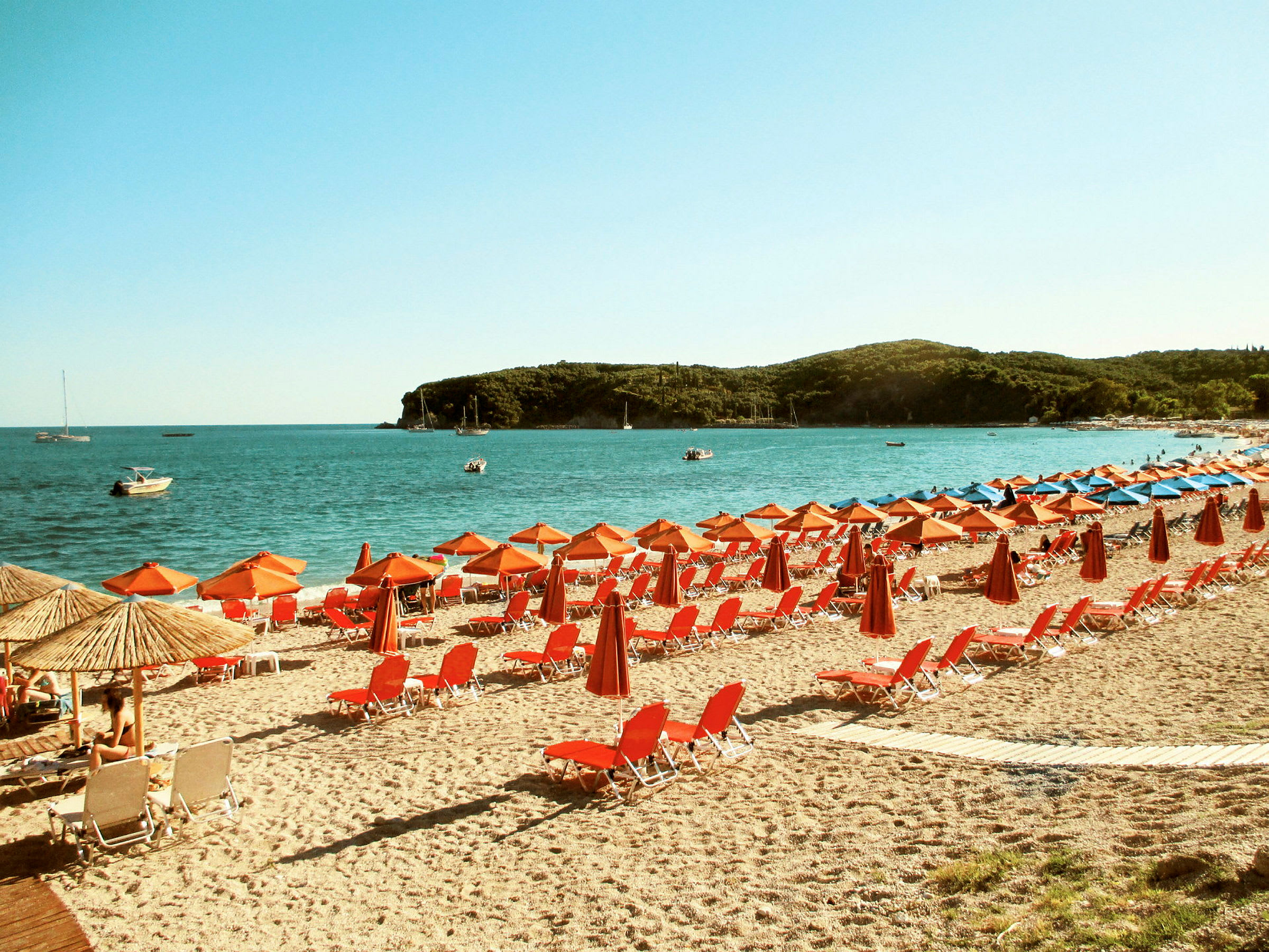 Strand med røde solsenger og parasoller ved kysten. (AI-generert tekst)