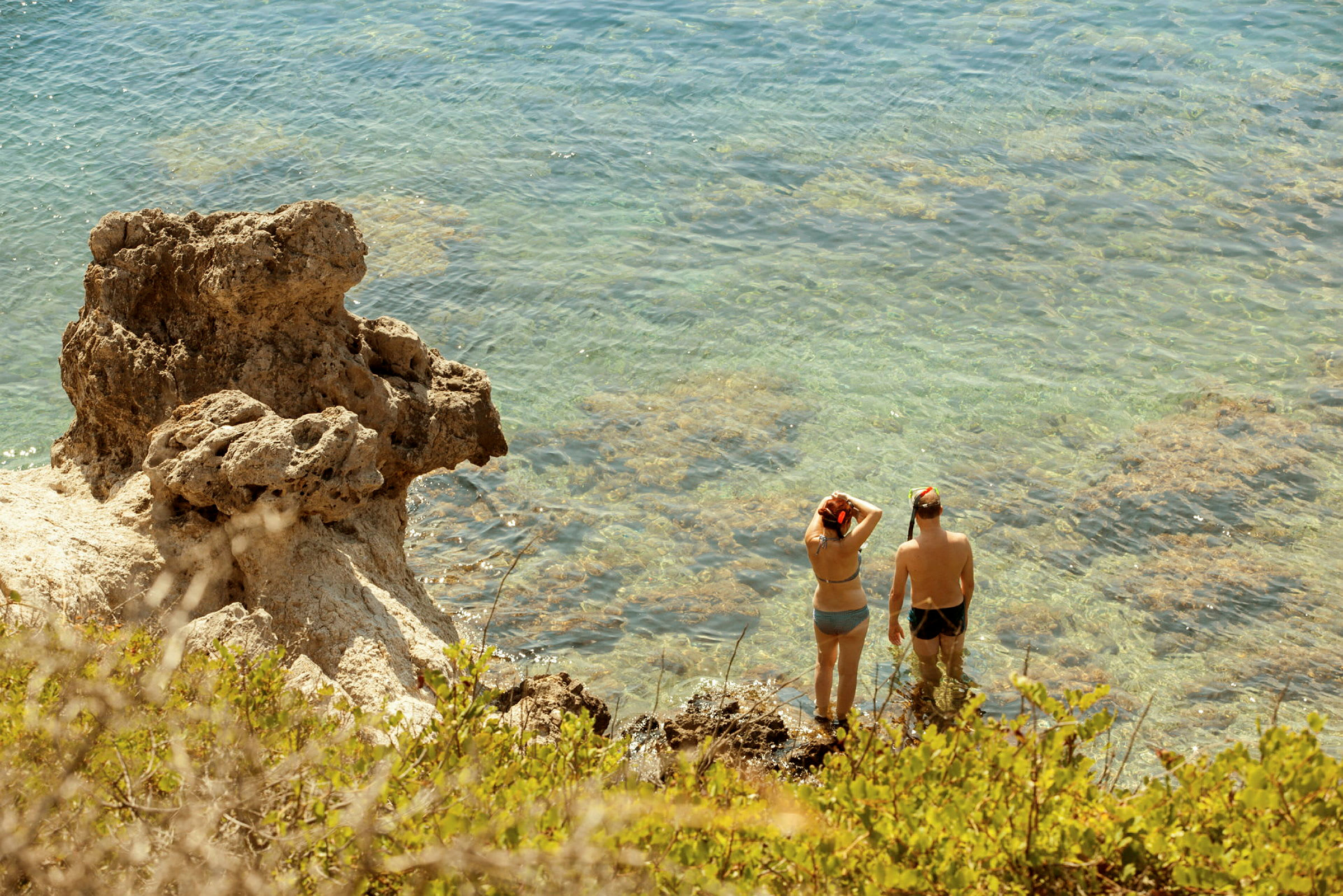 To personer står i klart vann ved en klippe, utstyrt med snorkelutstyr. (AI-generert tekst)