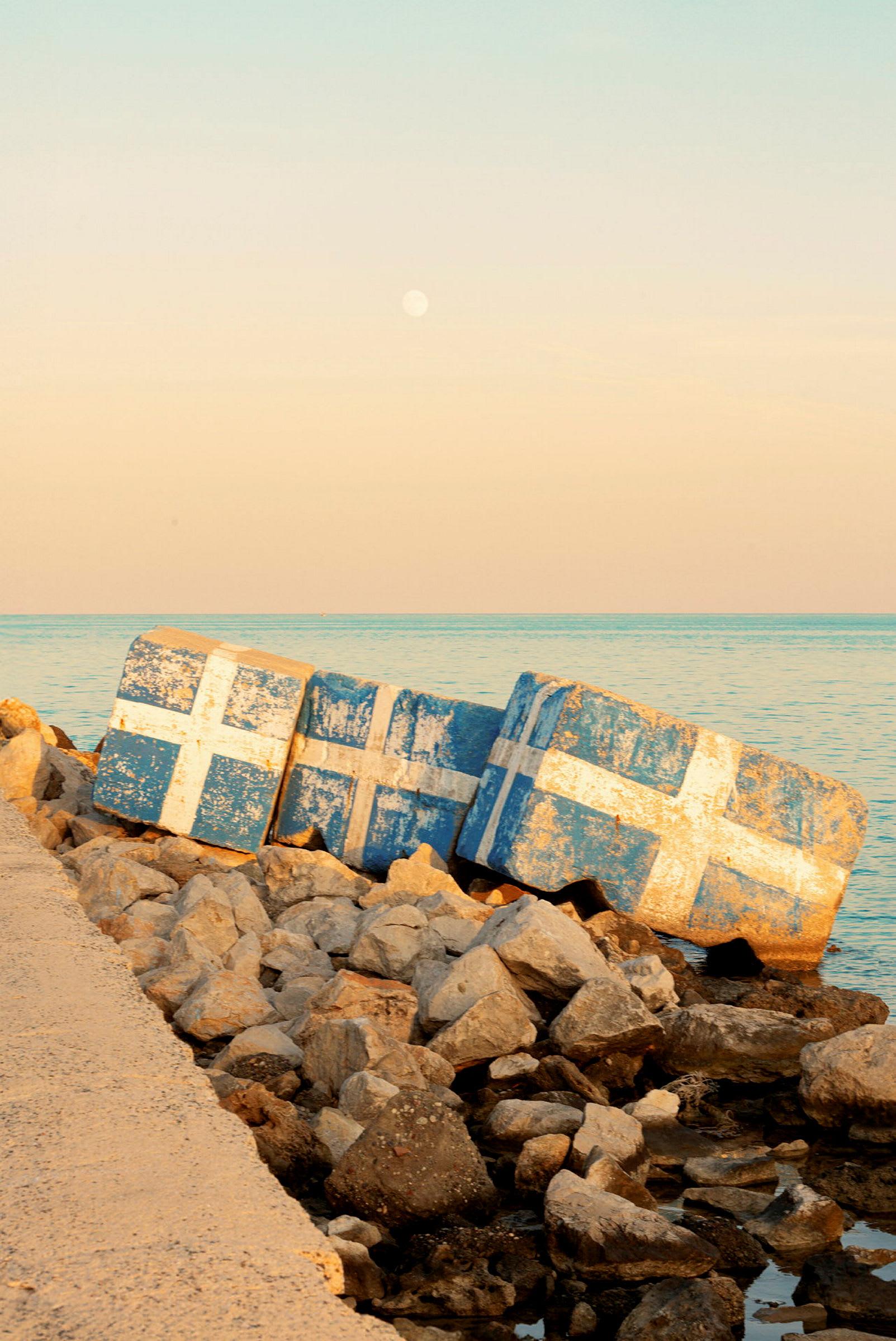 Betongblokker malt med hvite kors på blå bakgrunn ved en steinete strand. (AI-generert tekst)