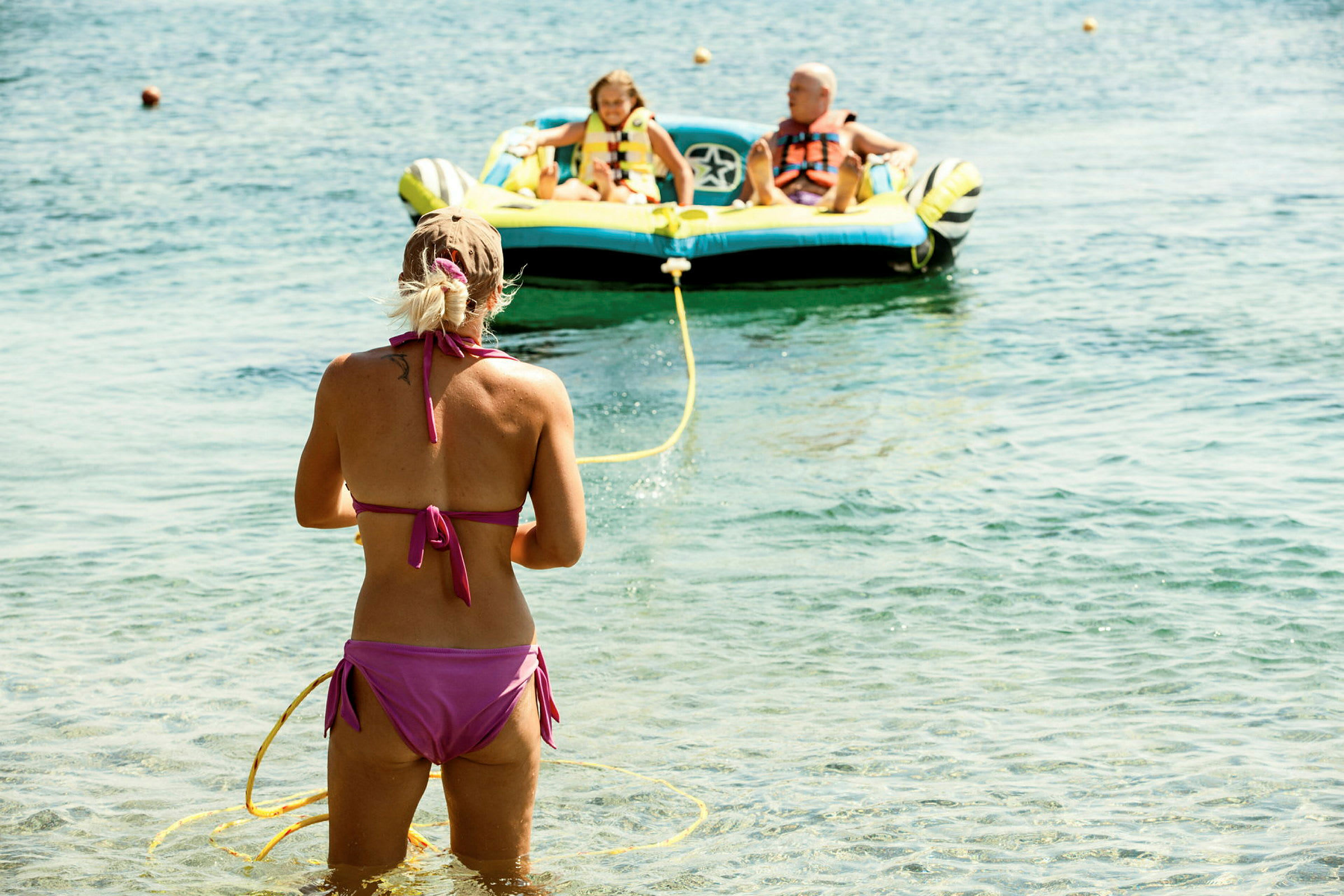 En person står i vannet og holder i et gult tau som fører til en oppblåsbar båt på havet. (AI-generert tekst)