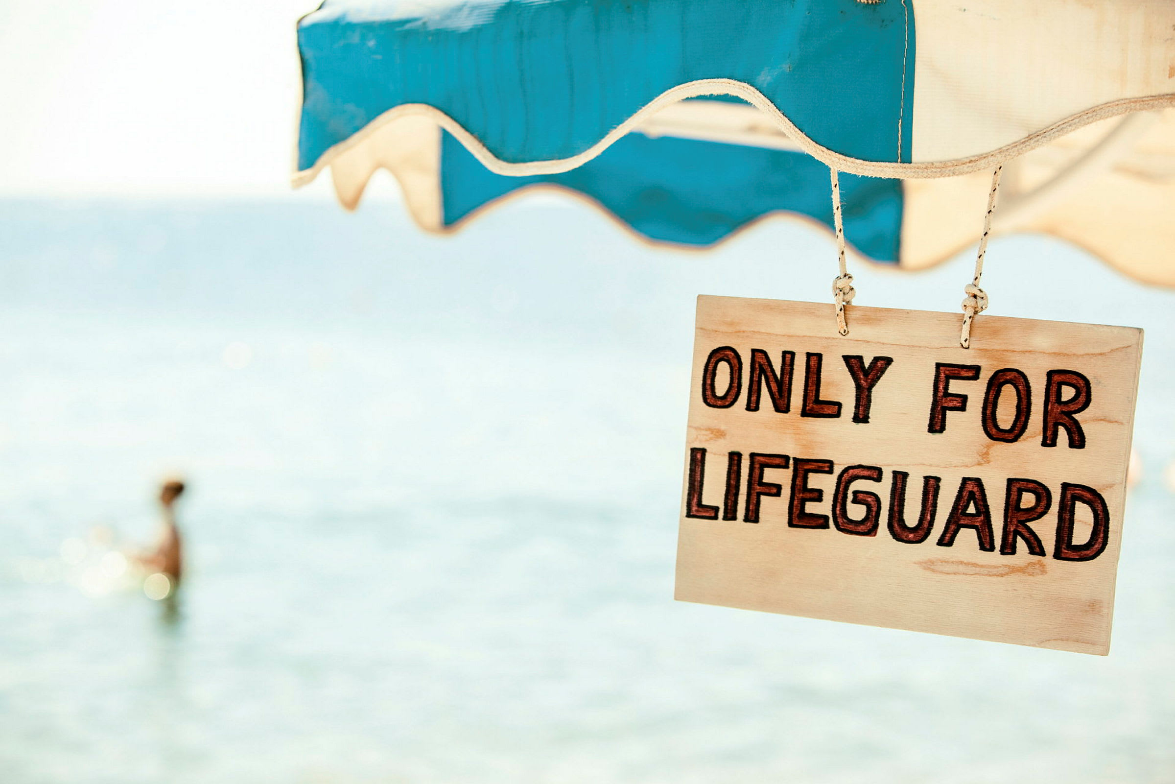 Skilt med teksten 'Only for lifeguard' hengt opp under en parasoll nær sjøen. (AI-generert tekst)