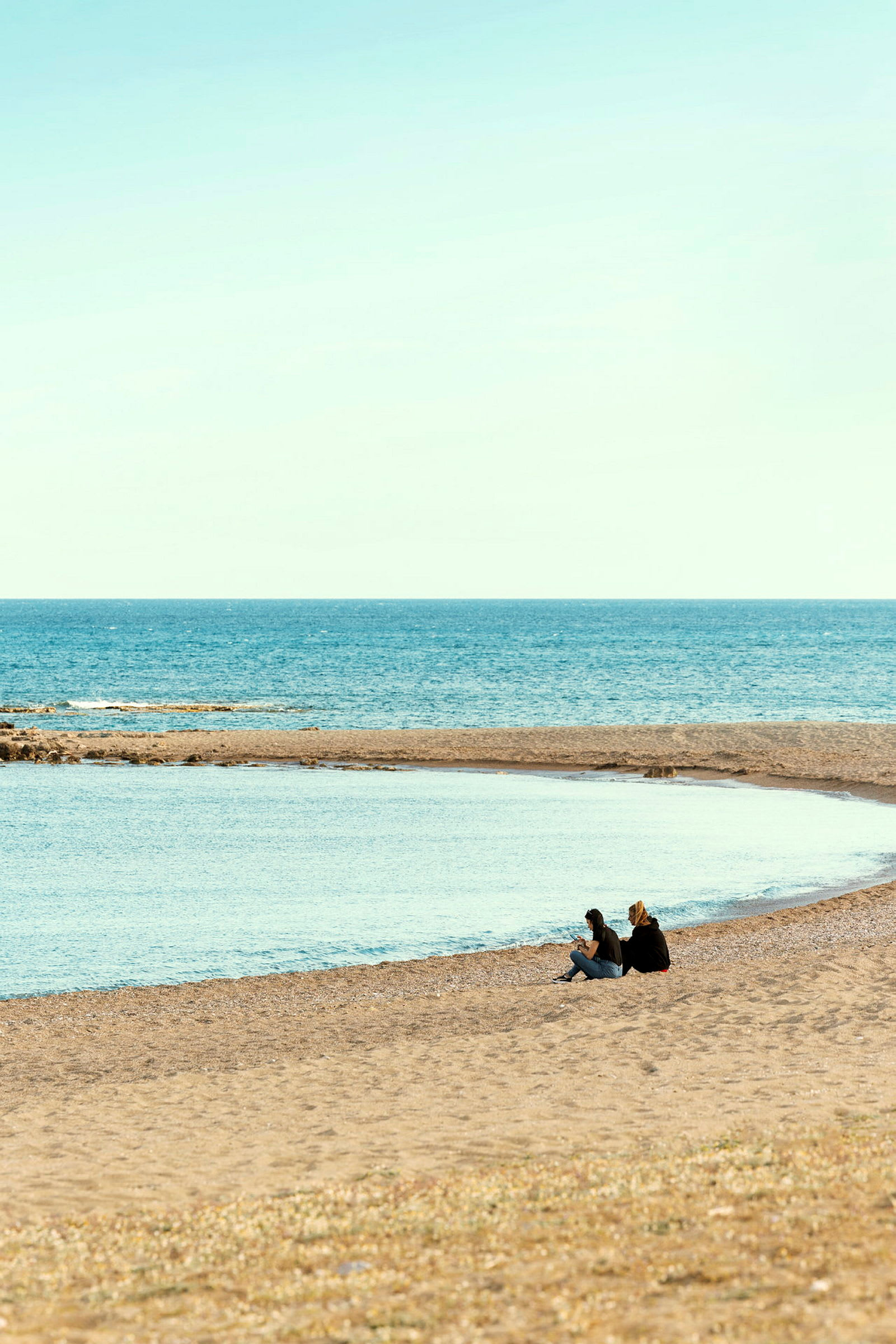 To personer sitter på en strand nær havet under klar himmel. (AI-generert tekst)