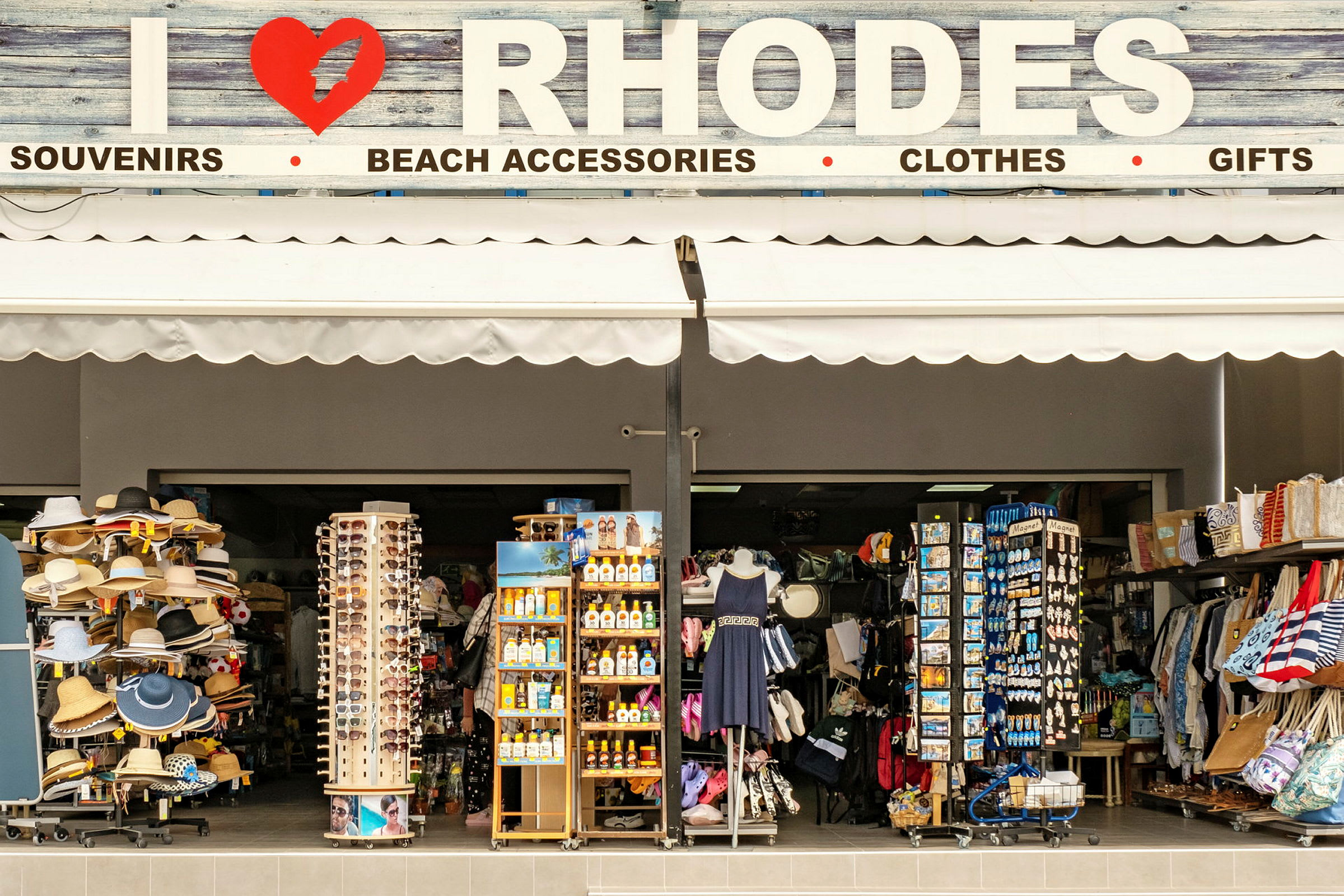 En butikk som selger suvenirer og strandutstyr med skiltet over som sier "I ❤ RHODOS". (AI-generert tekst)
