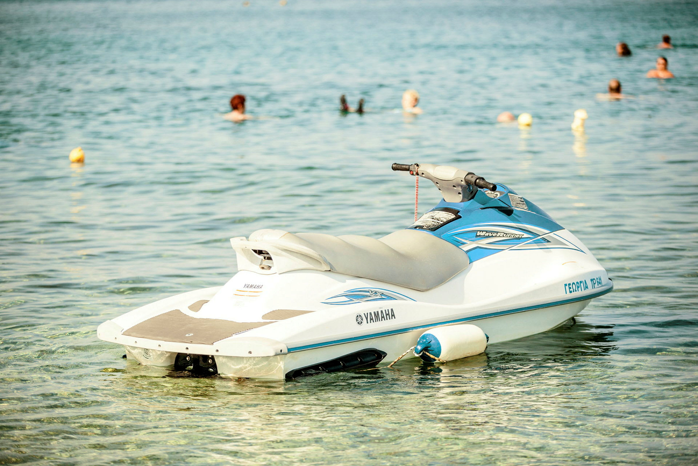 En jetski flyter på vannet med svømmende personer i bakgrunnen. (AI-generert tekst)