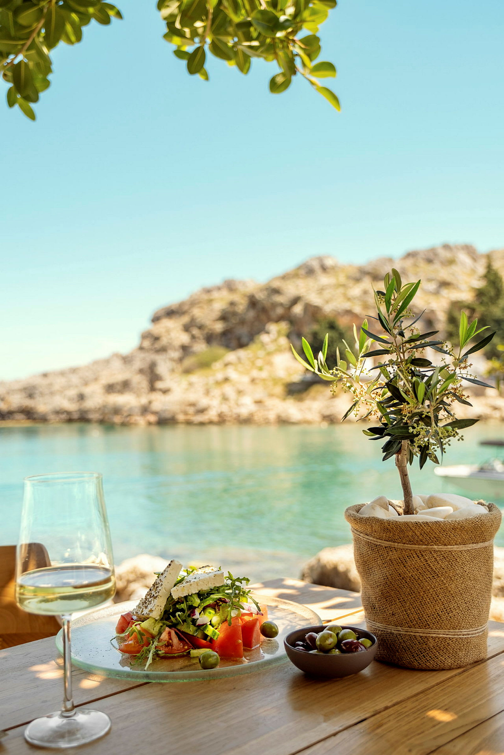 En lunsj med gresk salat, et glass vin og oliven ved havet. (AI-generert tekst)